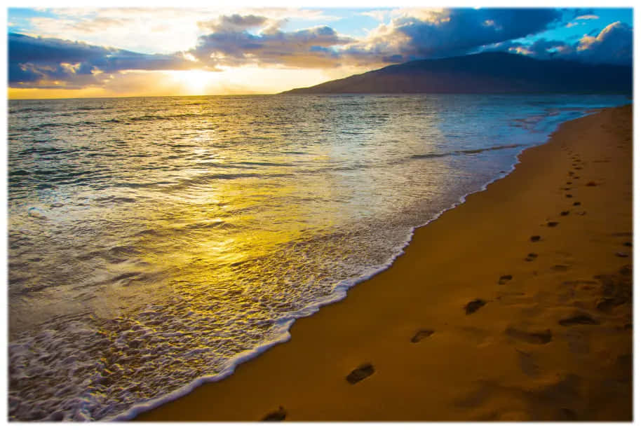夏威夷夕陽海灘沙灘風景 壁紙 — 金色夕陽將溫暖的光線投射在拍打沙灘的海浪上，沙灘上的腳印通往遠山。