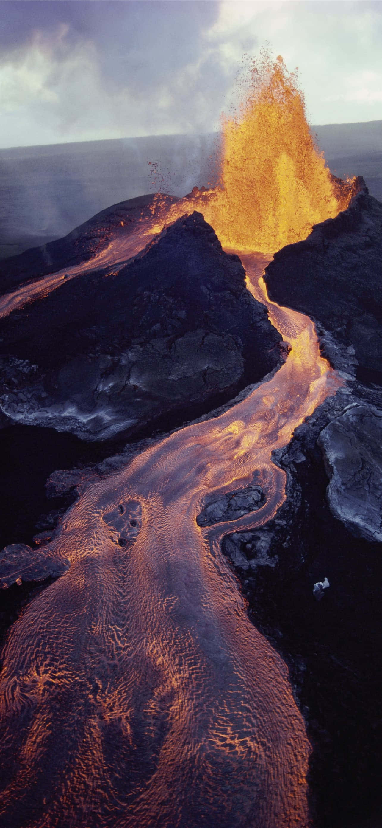 夏威夷火山國家公園火山噴發的壯麗美景 壁紙 — 火山爆發的鳥瞰圖，熾熱的橙色熔岩沿著崎嶇的黑色岩石流入海洋。