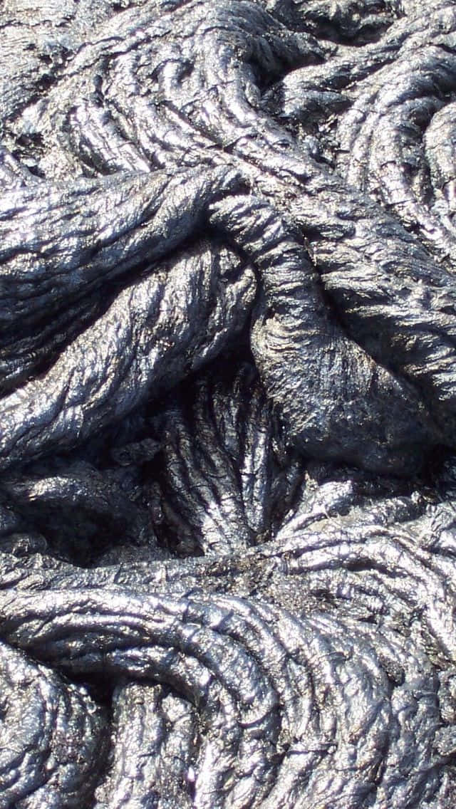 夏威夷火山國家公園火成岩特寫 壁紙 — 冷卻熔岩的近距離特寫，在明亮光線下呈現複雜扭曲紋理和金屬銀色亮點。