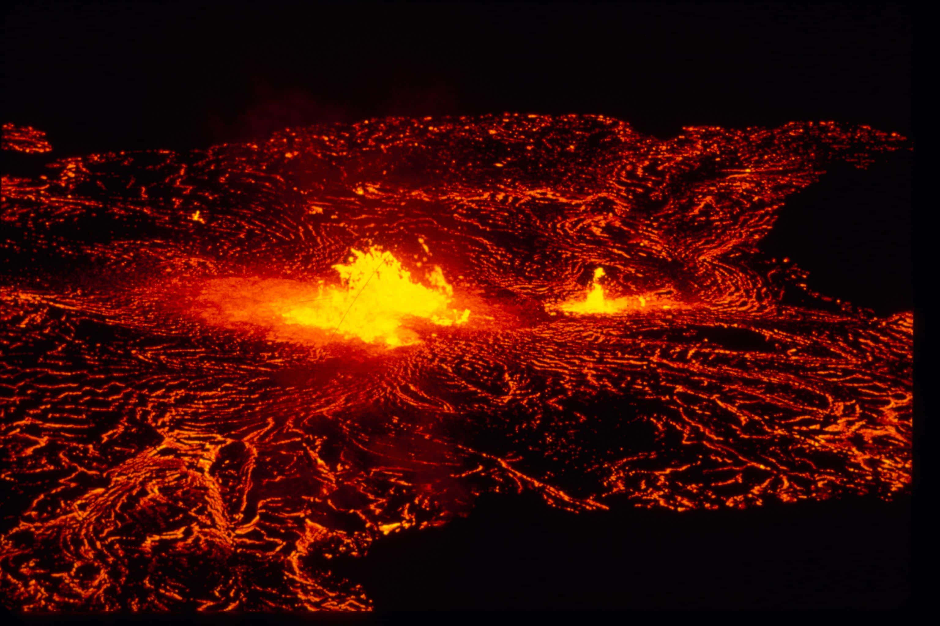 夏威夷火山國家公園熔岩之海 壁紙 — 夜間火山爆發，發光的橙色熔岩流過黑暗的景觀。