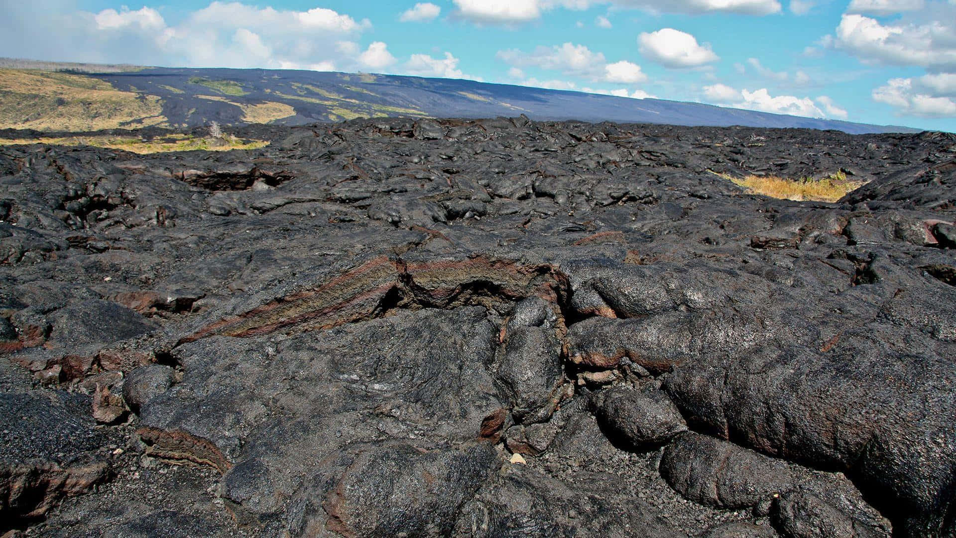 夏威夷火山國家公園黑岩地貌 壁紙 — 一片廣闊的冷卻黑色熔岩岩石在明亮的藍天下伸展，點綴著散落的白色雲朵。