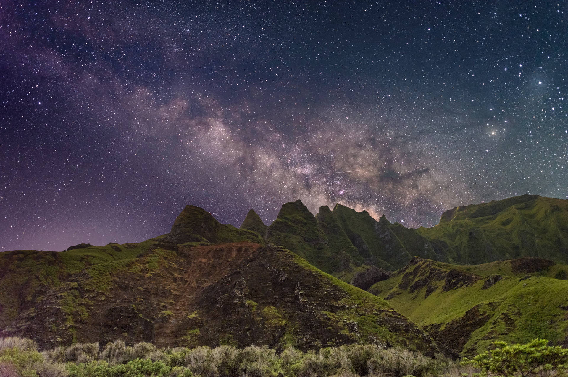 在繁星點點的夜空下，崎嶇的綠色山脈，銀河清晰可見。
