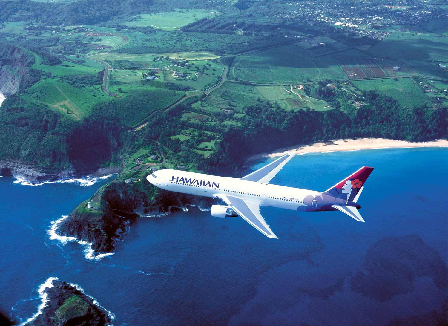 夏威夷航空飛機飛越熱帶島嶼，島上有綠色山丘和藍色海洋。