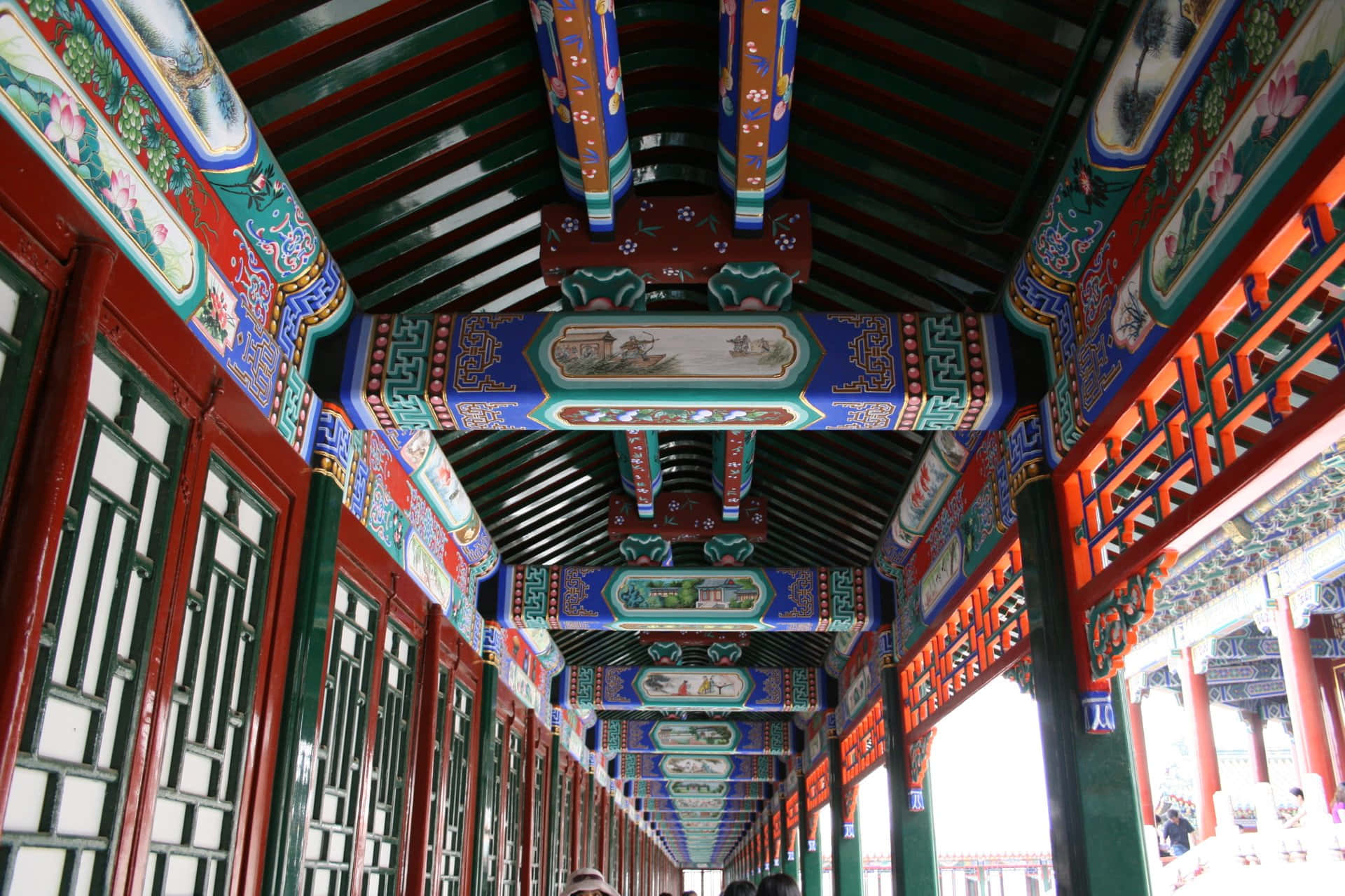 夏日宮殿的廊頂 壁紙 — 一條充滿活力的傳統中式走廊，帶有精緻彩繪的橫樑和紅色漆柱，延伸至遠方。