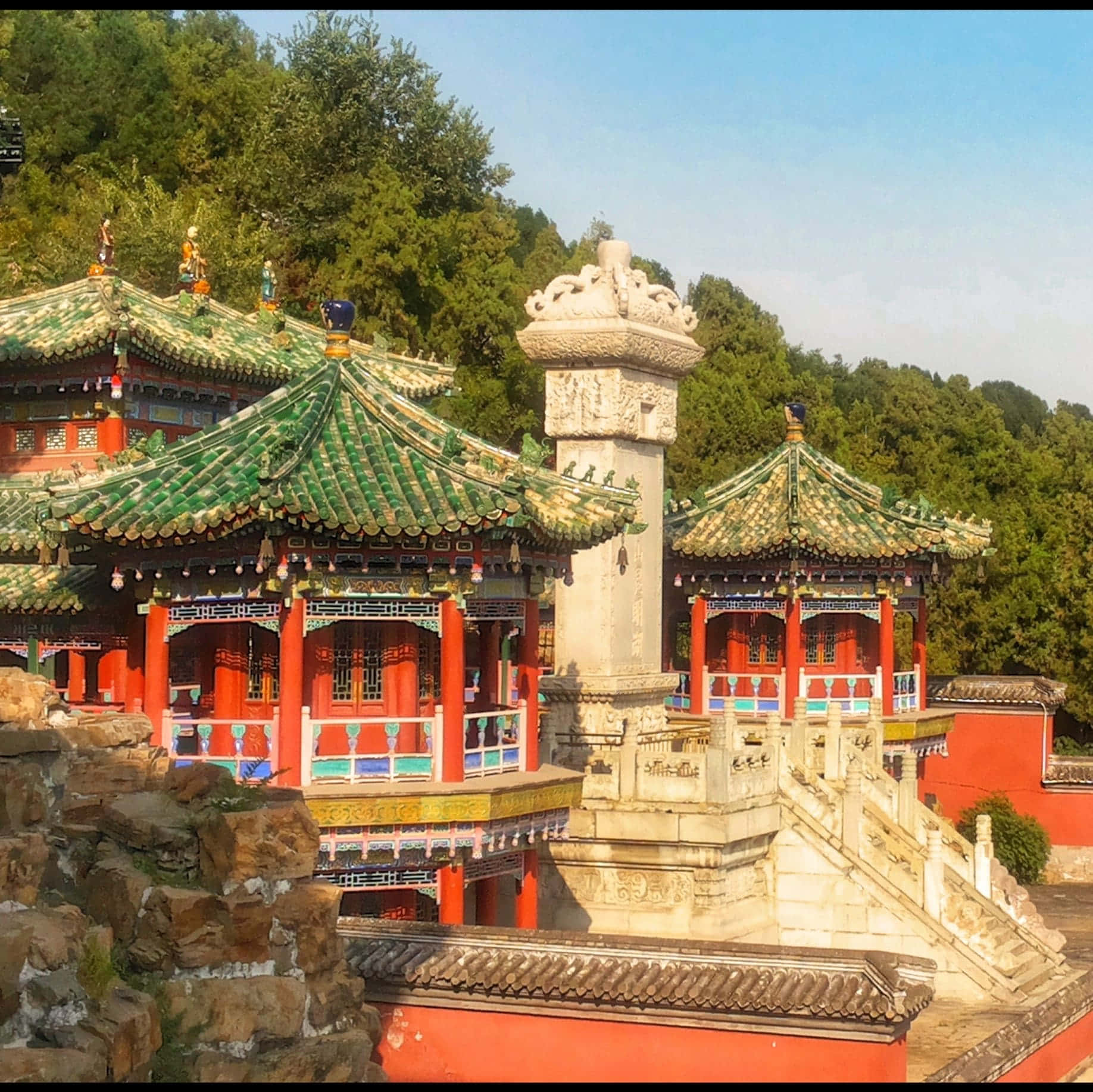 夏日宮殿美麗的外觀 壁紙 — 傳統中式寺廟，綠色瓦頂和紅色柱子，坐落在茂密的綠樹叢中，天空清澈湛藍。