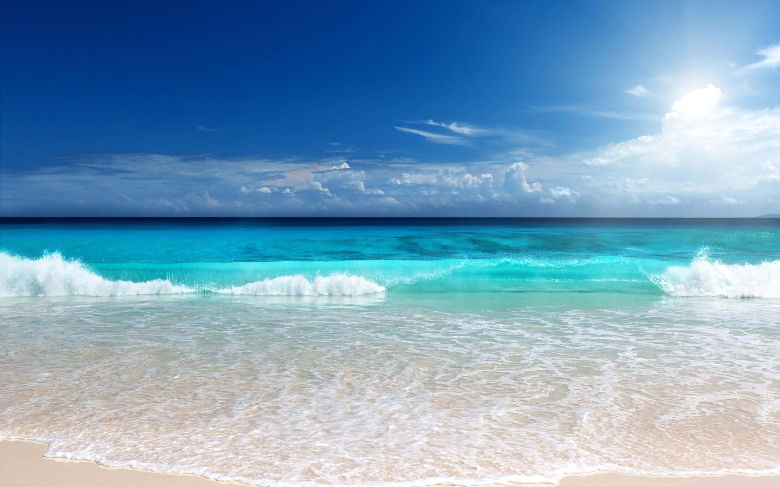 夏日熱帶海灘風景 壁紙 — 陽光在蔚藍的海浪上閃爍，海浪拍打著純淨的白色沙灘，上方是廣闊的藍天。