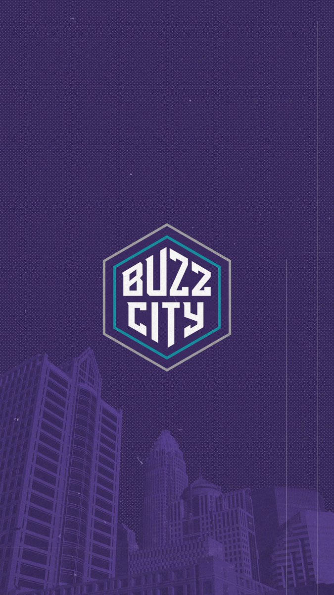 夏洛特黃蜂隊 Buzz City 壁紙 — 夜晚的紫色風格化城市景觀，摩天大樓上方中央有一個發光的六邊形「Buzz City」標誌。