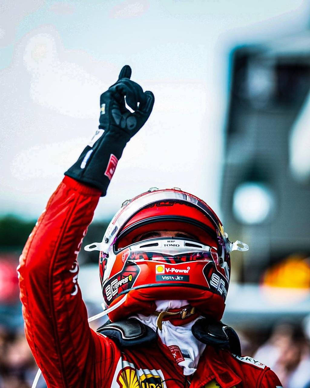 身穿紅色賽車服和頭盔的賽車手舉手慶祝勝利。