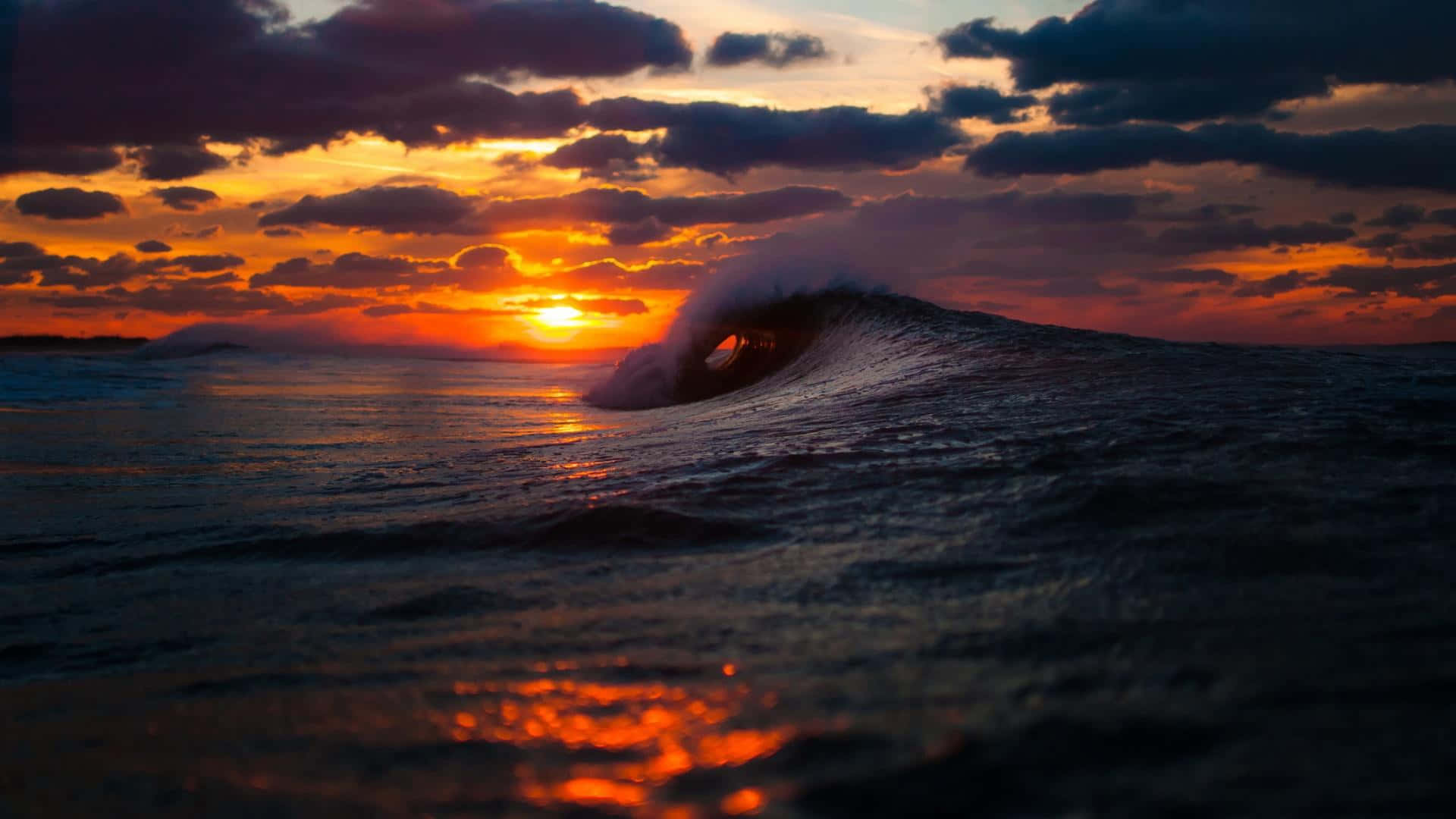 Sunset Ocean 桌布 壁紙 — 夕陽下，一道戲劇性的海浪完美捲成筒狀，上方有火橙色和紫色的雲彩。