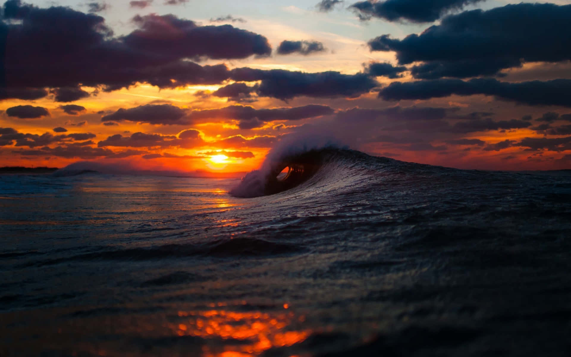 Sunset Wave 桌布 壁紙 — 夕陽下，一道戲劇性的海浪捲成完美的管狀，上方有火熱的橙色和紫色雲彩。