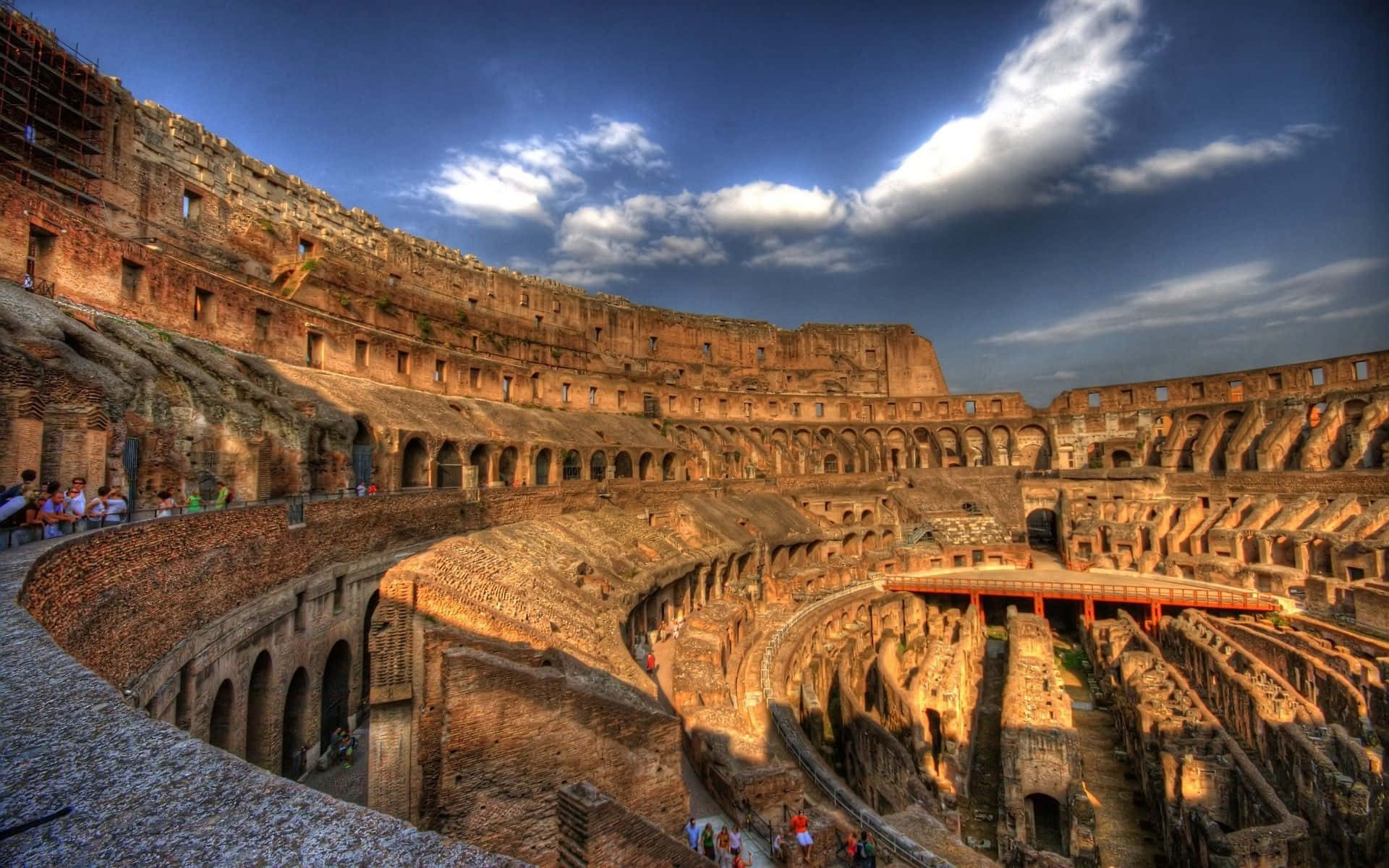 Rome 桌布 壁紙 — 夕陽下古羅馬競技場的戲劇性景觀，遊客在鮮豔的藍天下探索其巨大的石頭廢墟。
