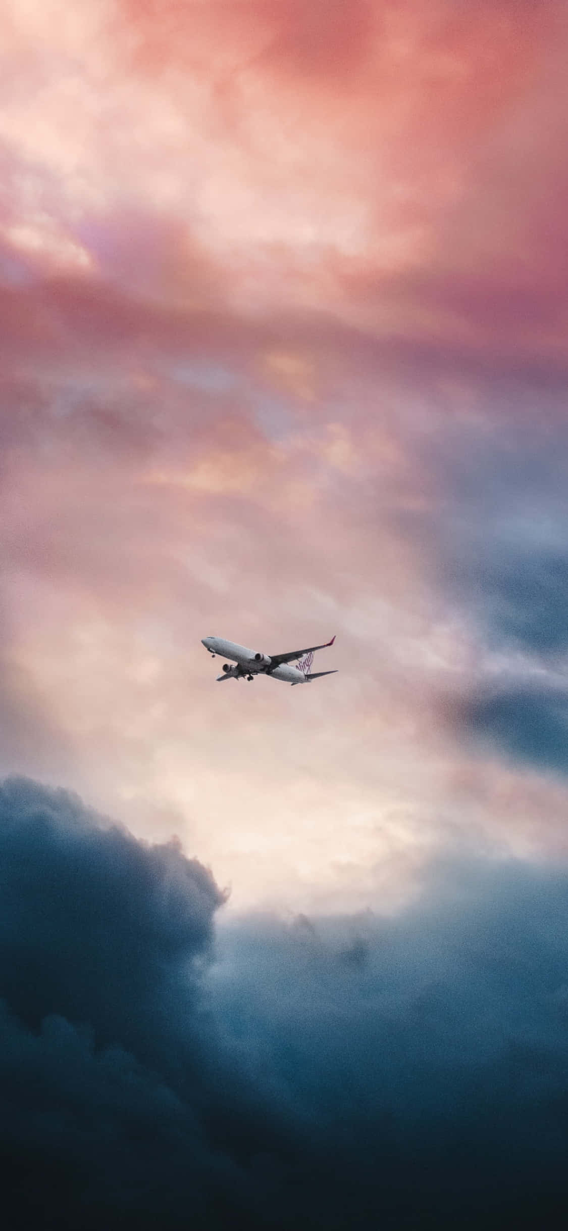 夕陽下小型飛機的壯麗景象 壁紙 — 一架客機在暮色中翱翔，穿過由粉紅、橙色和深藍色雲彩繪成的戲劇性天空。