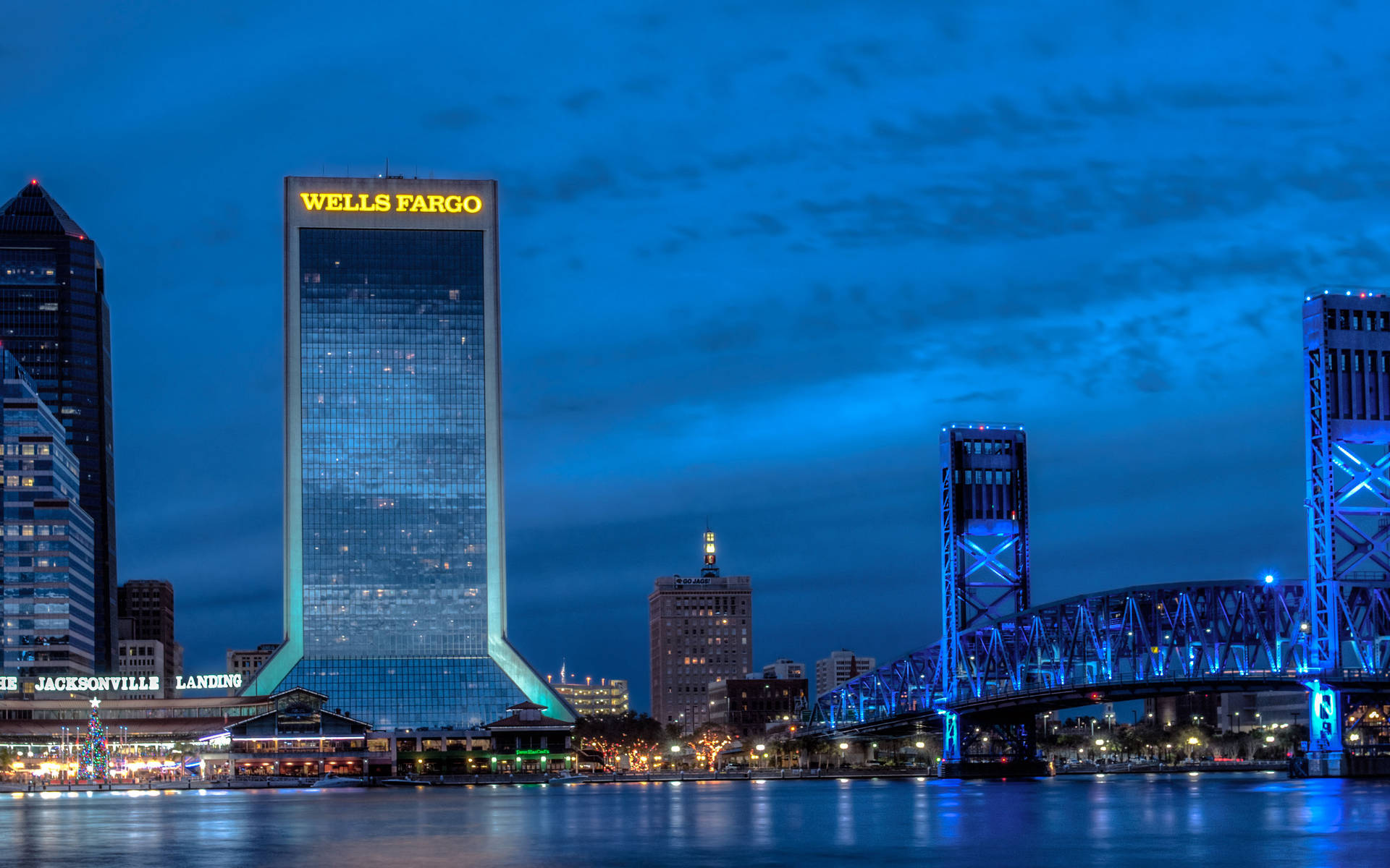 夕陽下的壯麗 Wells Fargo 大樓 壁紙 — 黃昏時分充滿活力的城市天際線，發光的 Wells Fargo 塔和藍色燈光的橋樑倒映在平靜的水面上。