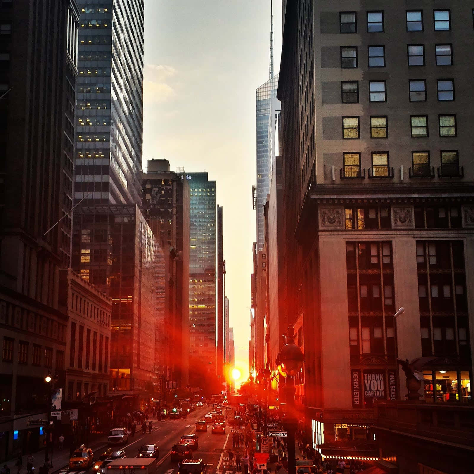 高樓之間的夕陽照亮了充滿汽車和行人的繁華城市街道。