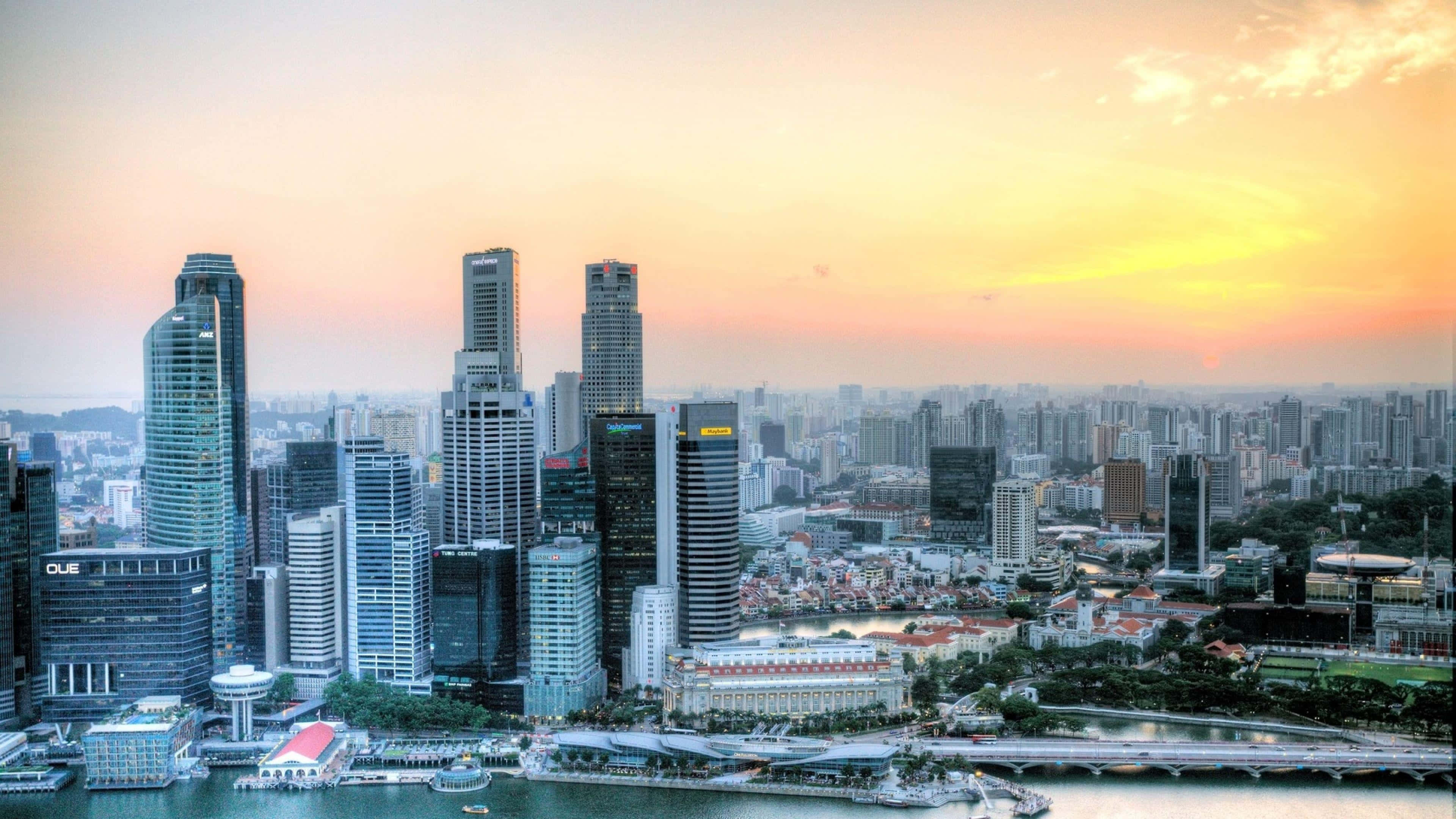 Singapore 桌布 壁紙 — 夕陽以溫暖的金色光芒沐浴新加坡的天際線，現代摩天大樓在水濱之上聳立。