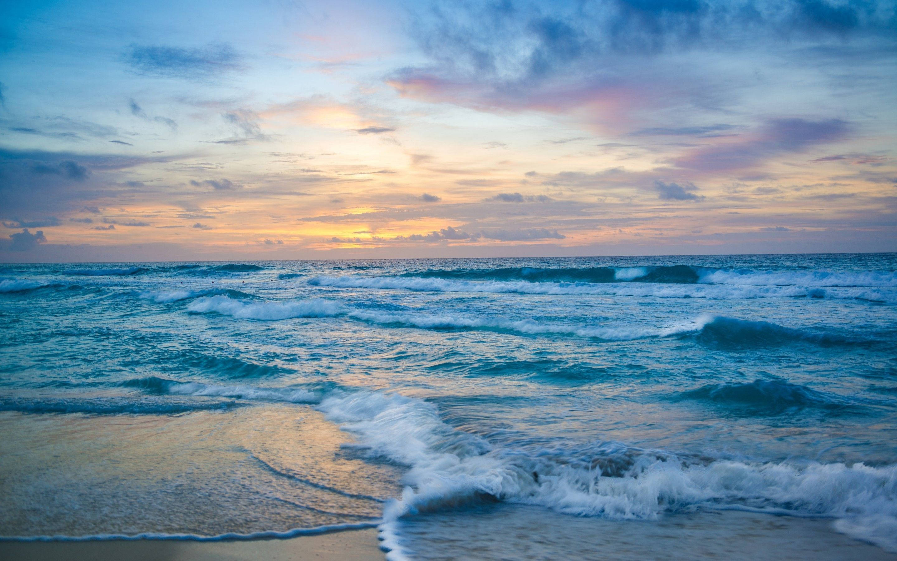 waves 桌布 壁紙 — 夕陽以溫暖色調塗抹天空，海浪在戲劇性的雲層密佈地平線下拍打沙灘。