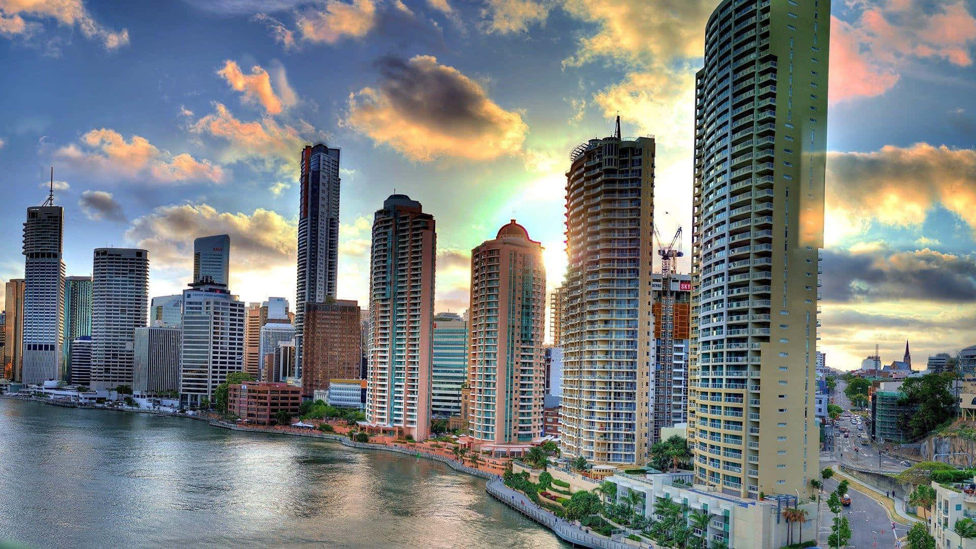 Buildings 桌布 壁紙 — 夕陽以金色光芒沐浴現代城市天際線，雲彩在平靜的海濱上空劃過天際。