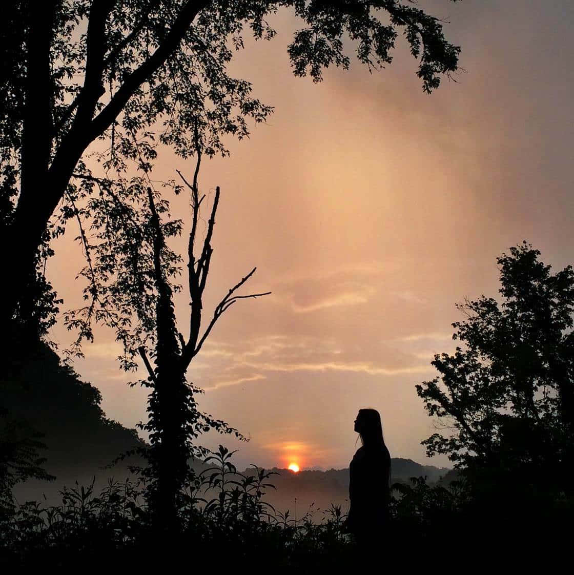 夕陽剪影自然風景 壁紙 — 一個人的剪影，站在日落時分的森林中，溫暖的橙色天空和霧氣繚繞的山丘。