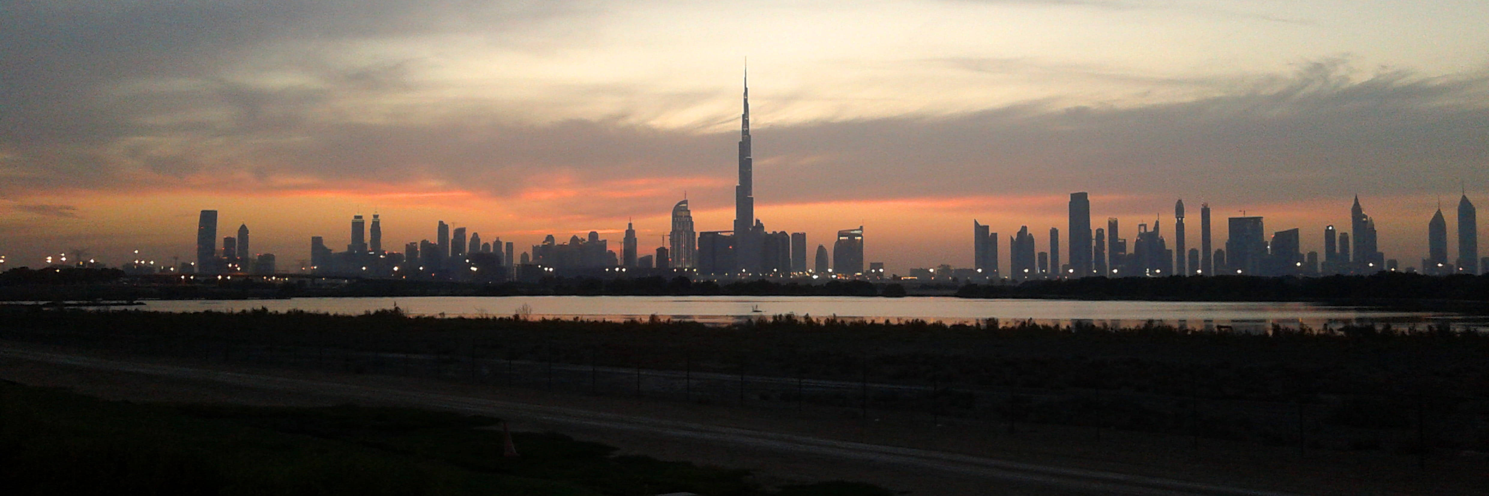 Dubai 桌布 壁紙 — 夕陽勾勒出杜拜的天際線，哈利法塔聳立在水面上，城市燈光開始閃爍。
