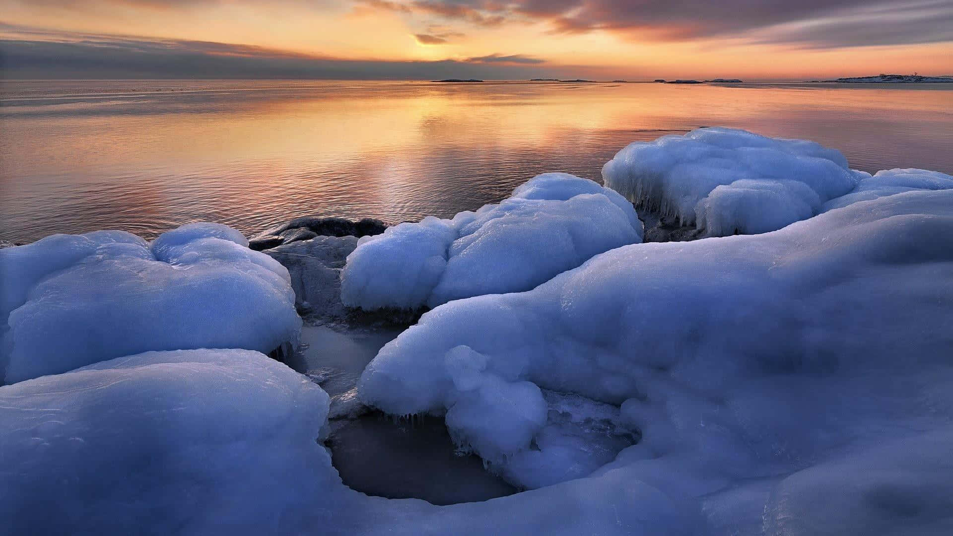Winter Beach 桌布 壁紙 — 夕陽在冬天的邊緣，將冰冷的岩石和寧靜的水面塗上溫暖的金色和冷藍色。