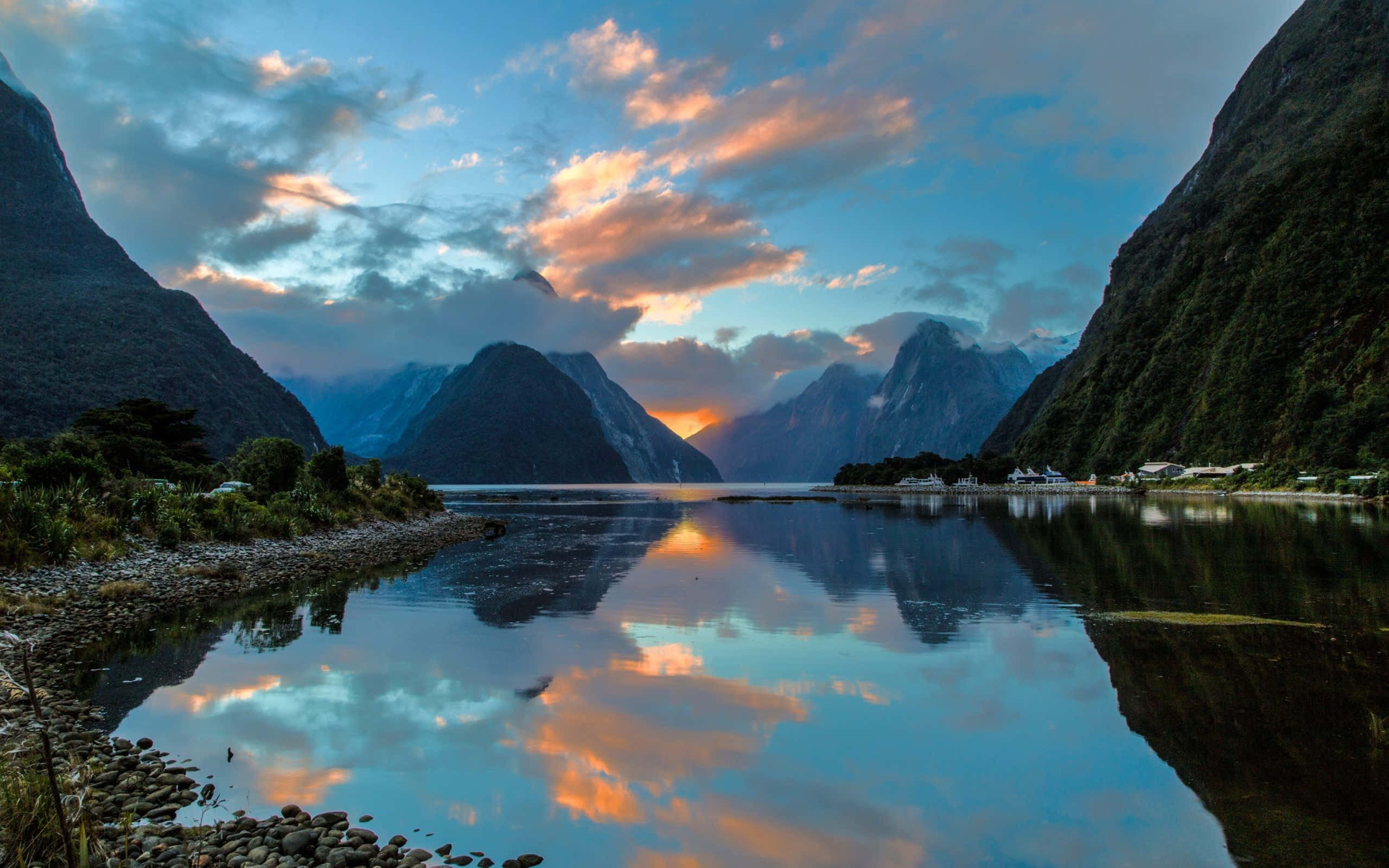 New Zealand 桌布 壁紙 — 夕陽將天空和山脈染成火熱的橙色和藍色，完美地倒映在平靜的峽灣水域中。