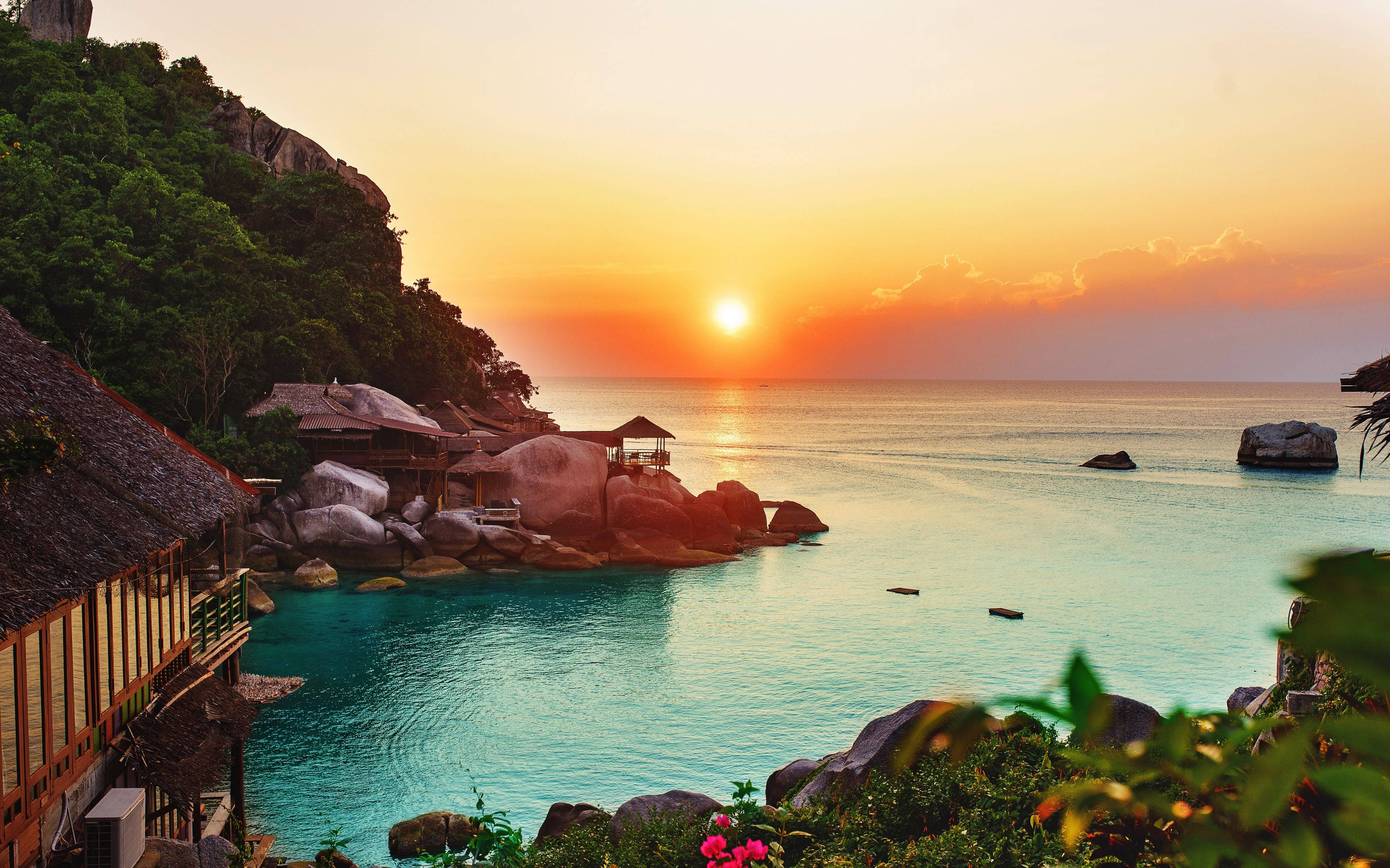 海洋 桌布 壁紙 — 夕陽將天空染成橙色，沉入叢林覆蓋的懸崖和木屋旁平靜的碧綠海水之上。