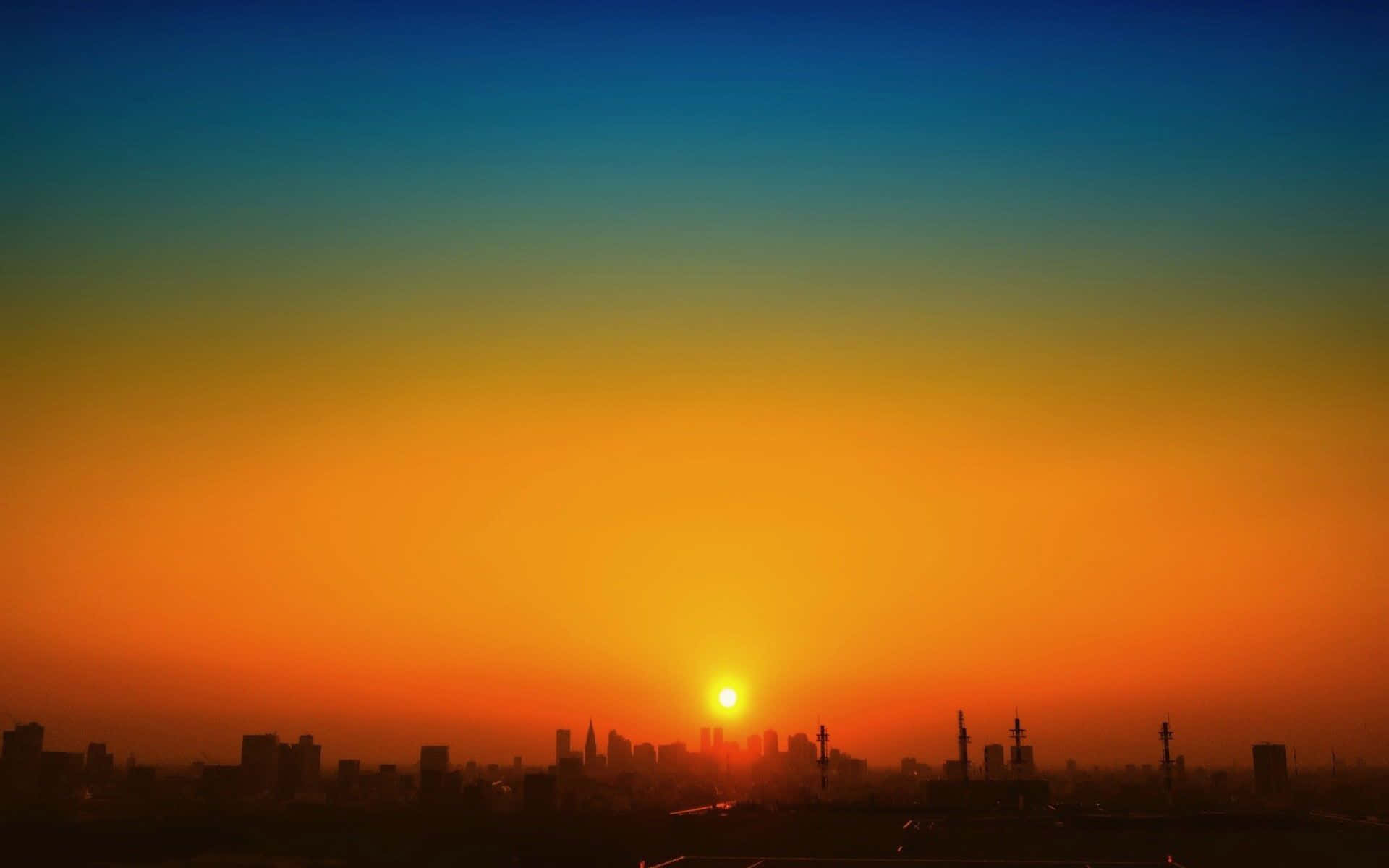 Orange Sunset 桌布 壁紙 — 夕陽將天空染成橙色和藍色，太陽在剪影般的城市天際線後落下。