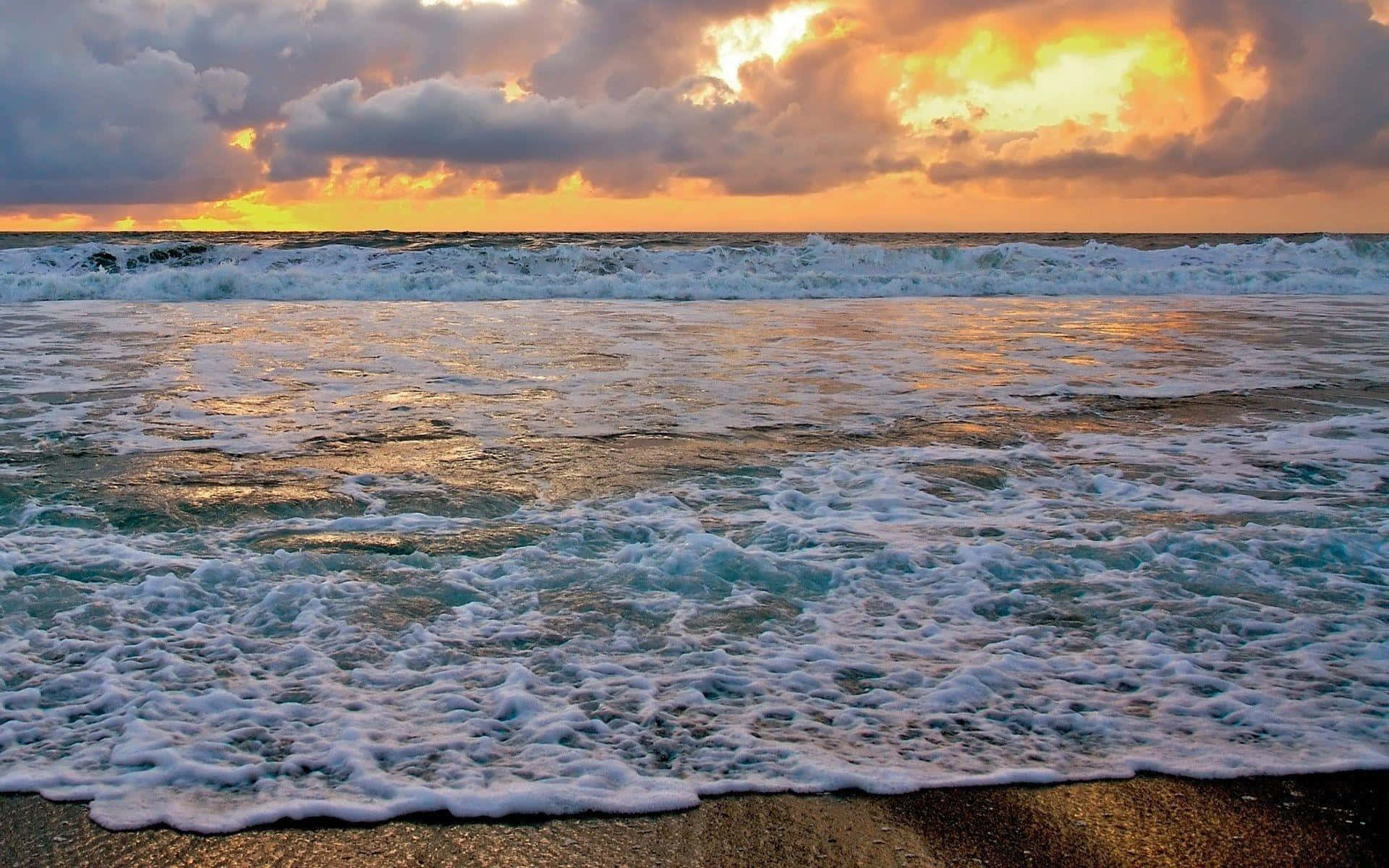 Beautiful Ocean 桌布 壁紙 — 夕陽將天空染成橙色和金色，海浪帶著白色泡沫拍打沙灘。