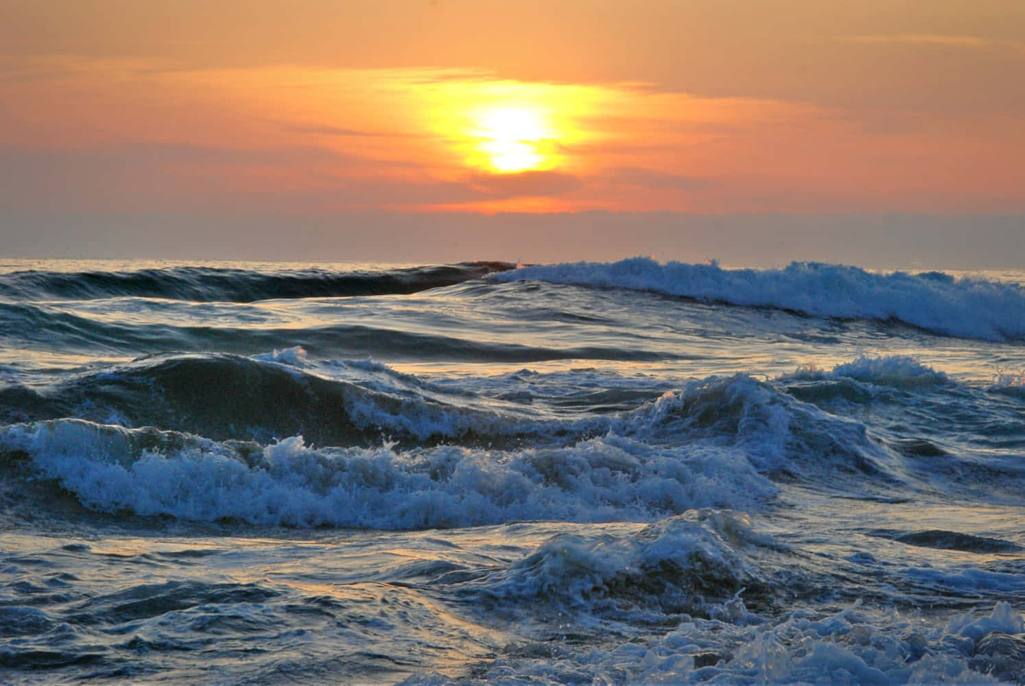 波浪 桌布 壁紙 — 夕陽將天空染成溫暖的橙色，海浪帶著白色泡沫拍打著地平線。