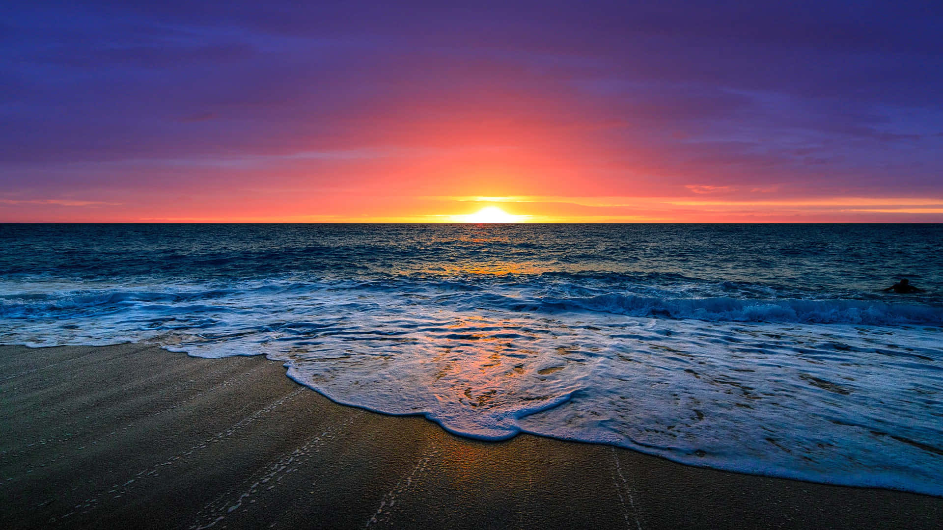 Beautiful Ocean 桌布 壁紙 — 夕陽將天空染成火橙色和深紫色，海浪拍打沙灘。