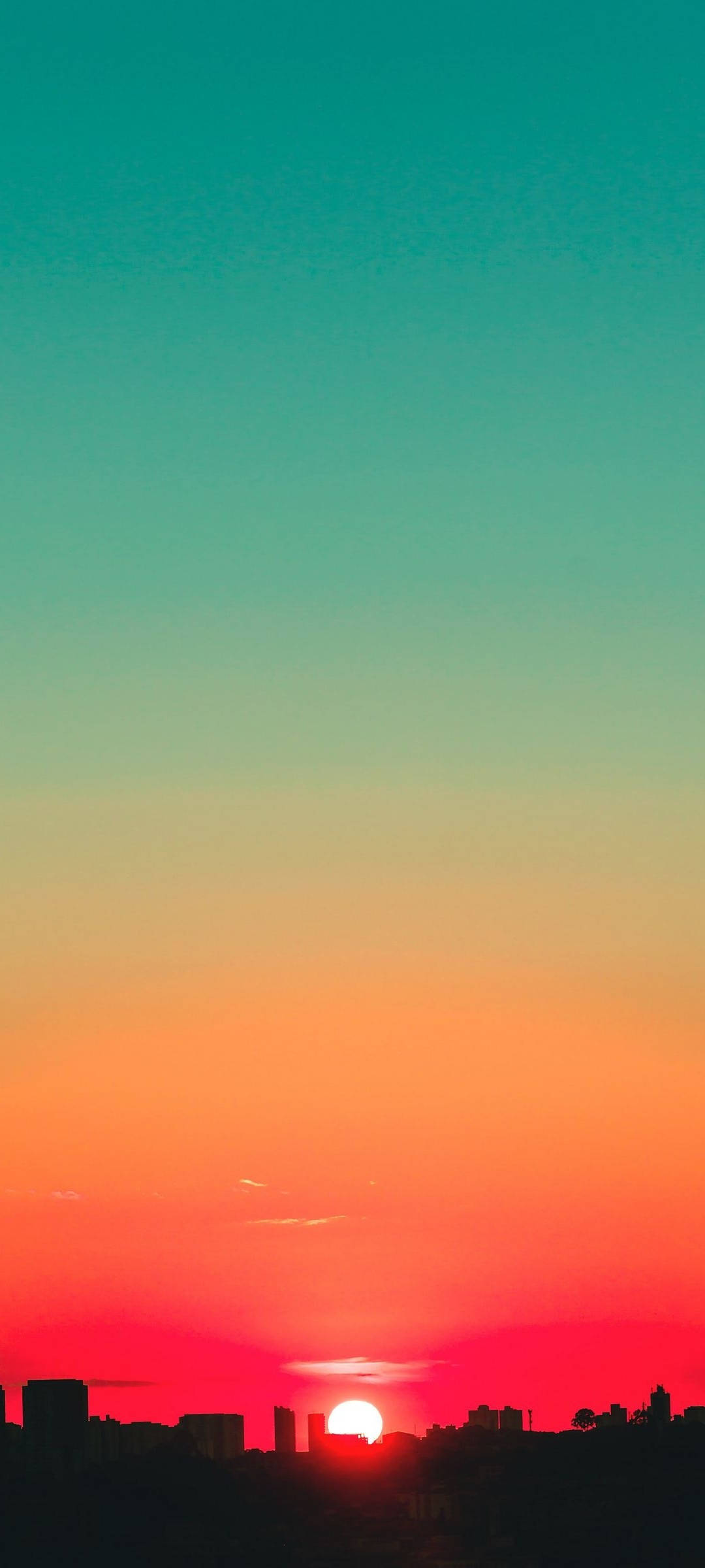 日落天空 桌布 壁紙 — 夕陽將天空染成火橙色和藍綠色，城市天際線的輪廓在夕陽下顯得格外鮮明。