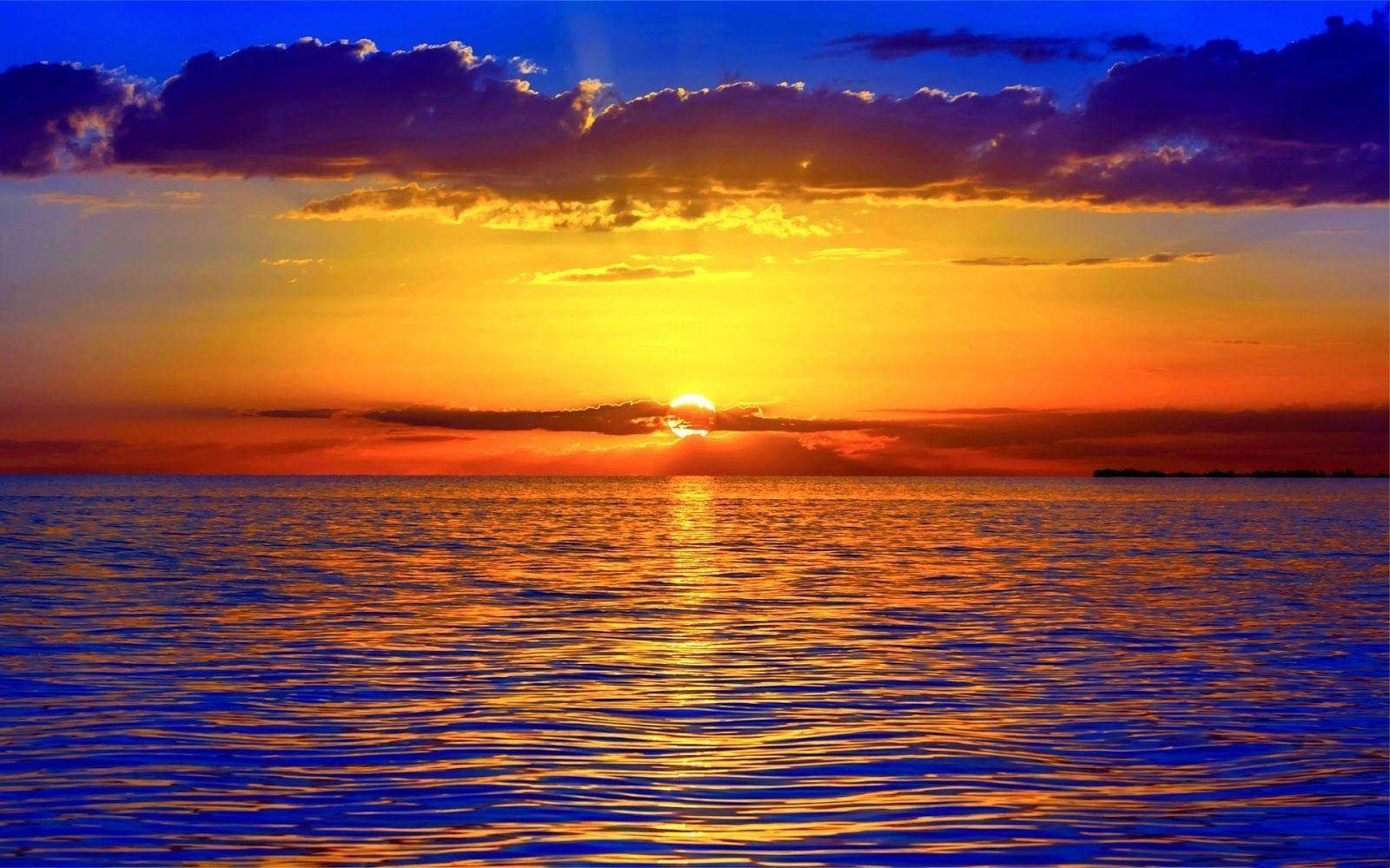 日落 桌布 壁紙 — 夕陽將天空染成火熱的橙色和深藍色，太陽在平靜的海洋上空沉入地平線。
