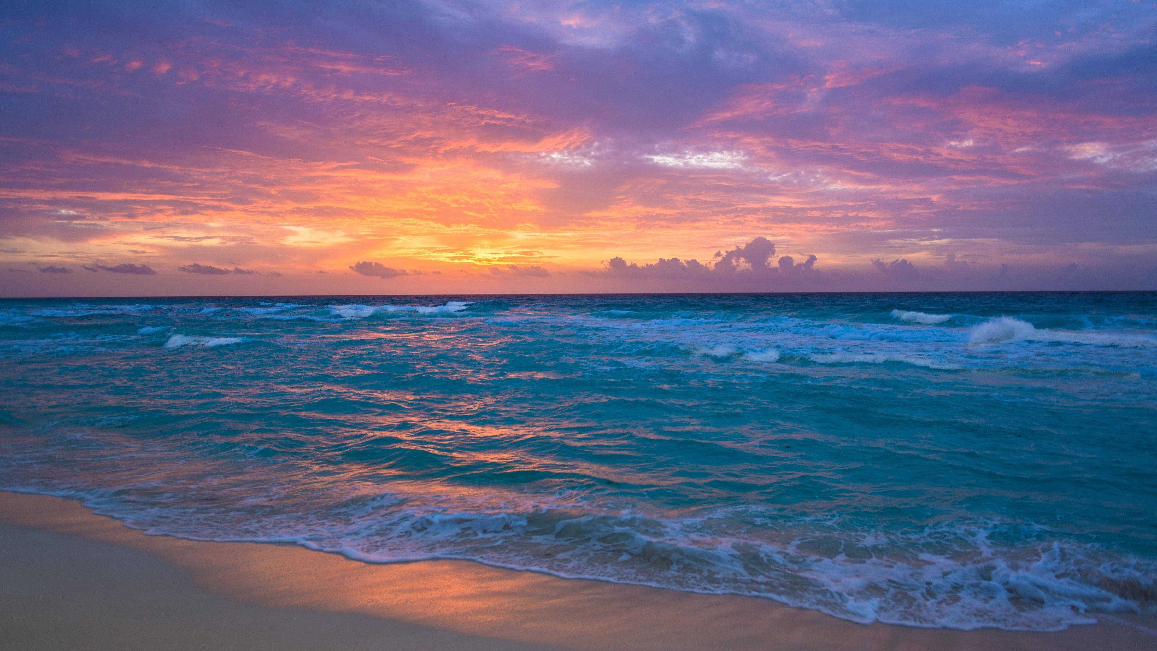 海洋 桌布 壁紙 — 夕陽將天空染成火熱的橙色和紫色，海浪拍打著金色的沙灘。