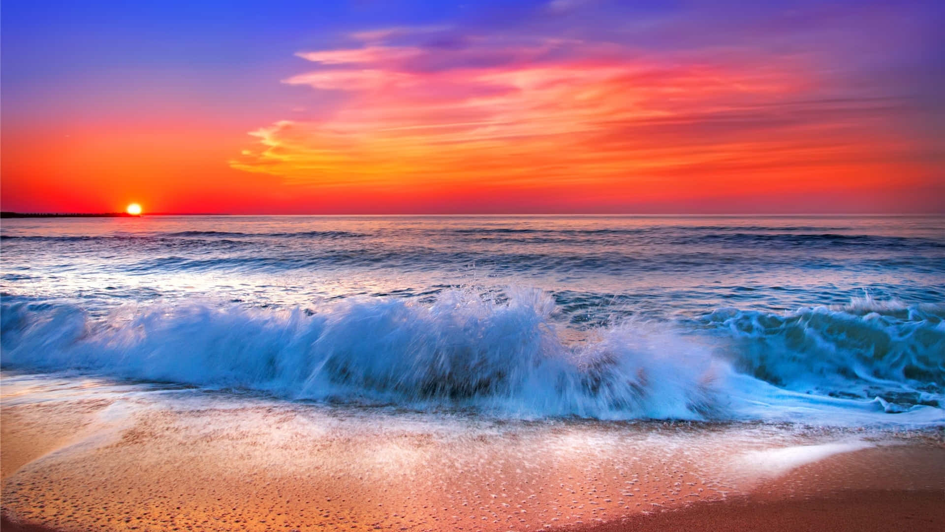 Sunset Wave 桌布 壁紙 — 夕陽將天空染成火熱的橙色和紫色，海浪拍打著沙灘。