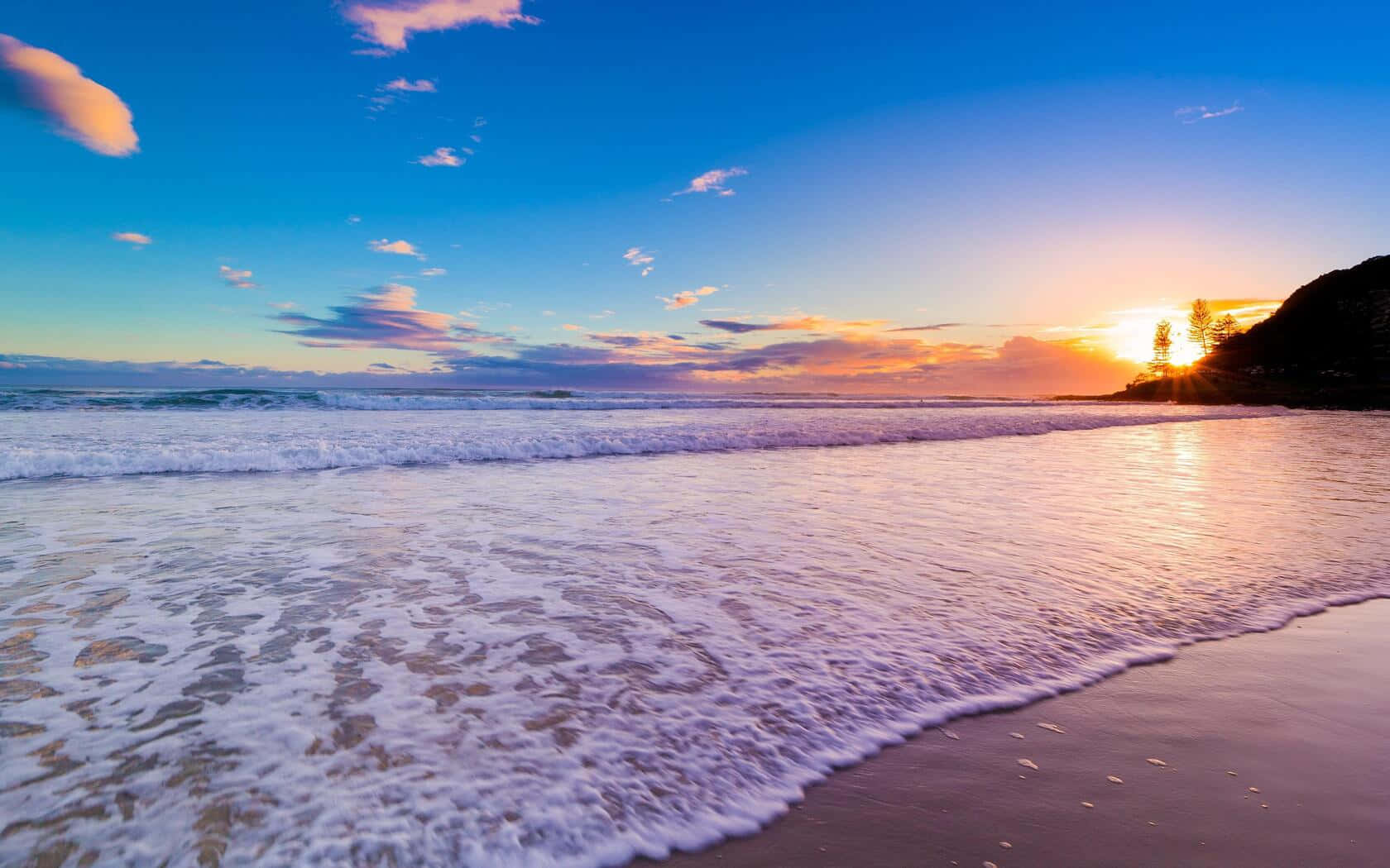 Beautiful Beach 桌布 壁紙 — 夕陽將天空染成火熱的橙色和藍色，海浪帶著泡沫衝擊沙灘。