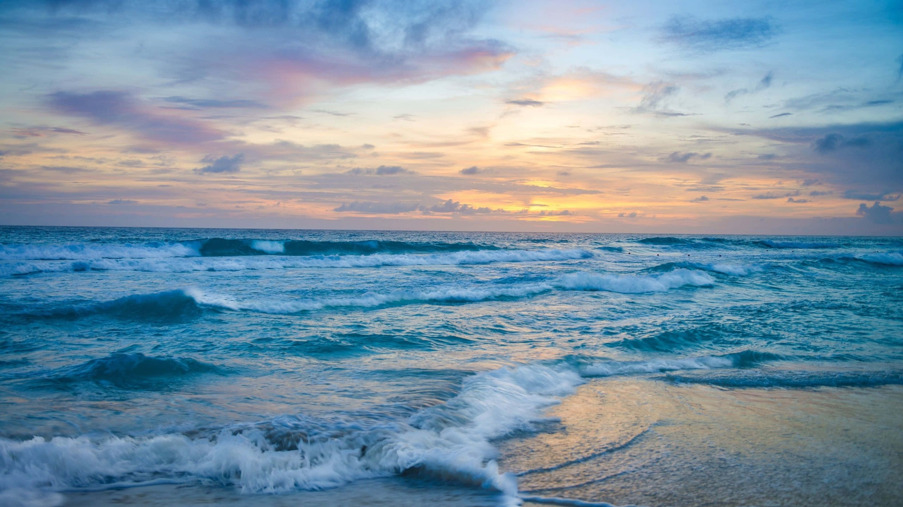 Aesthetic Beach 桌布 壁紙 — 夕陽將天空染成粉紅、金色和藍色，海浪拍打沙灘。