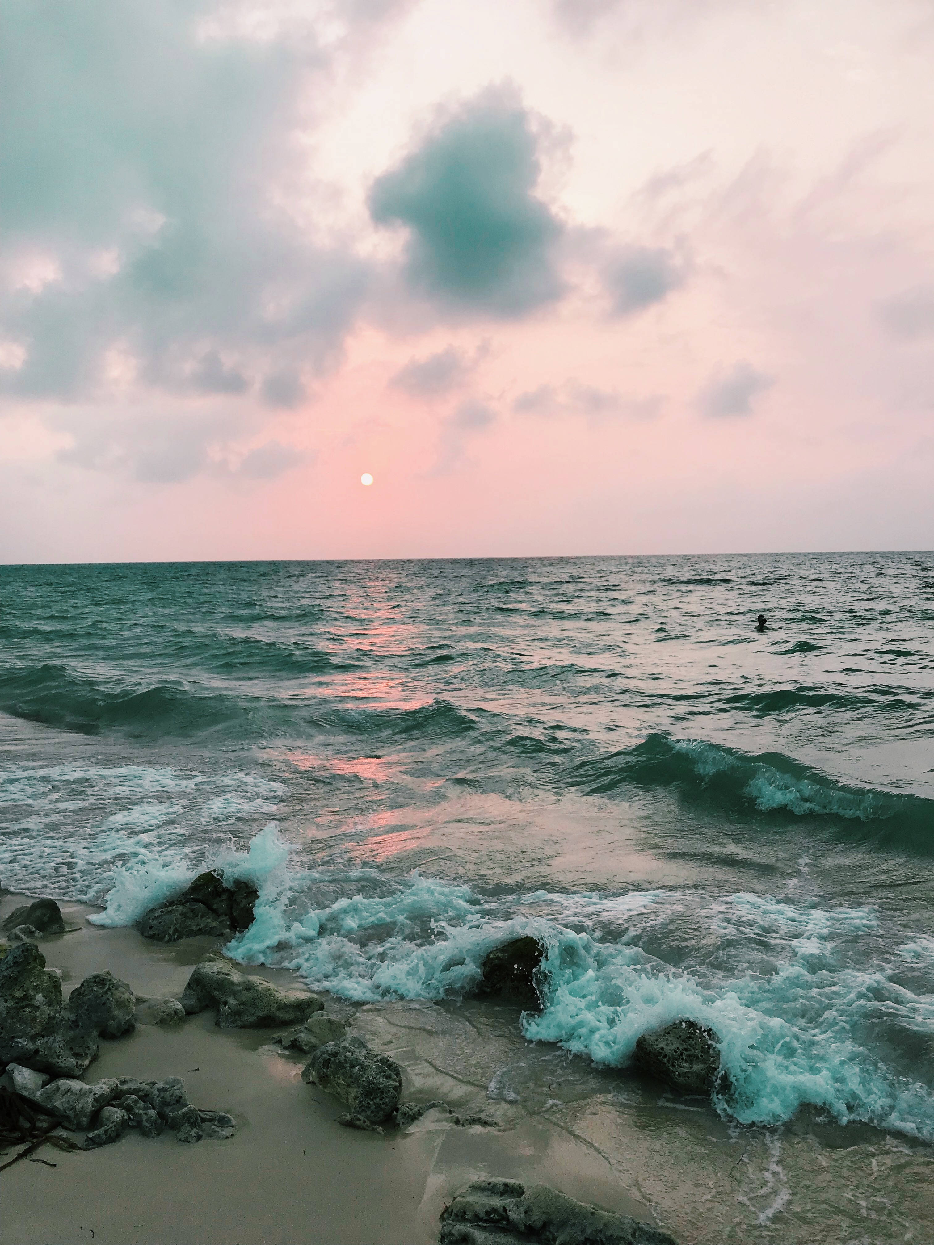 日落 桌布 壁紙 — 夕陽將天空染成粉紅色和藍綠色，海浪拍打岩石海岸。