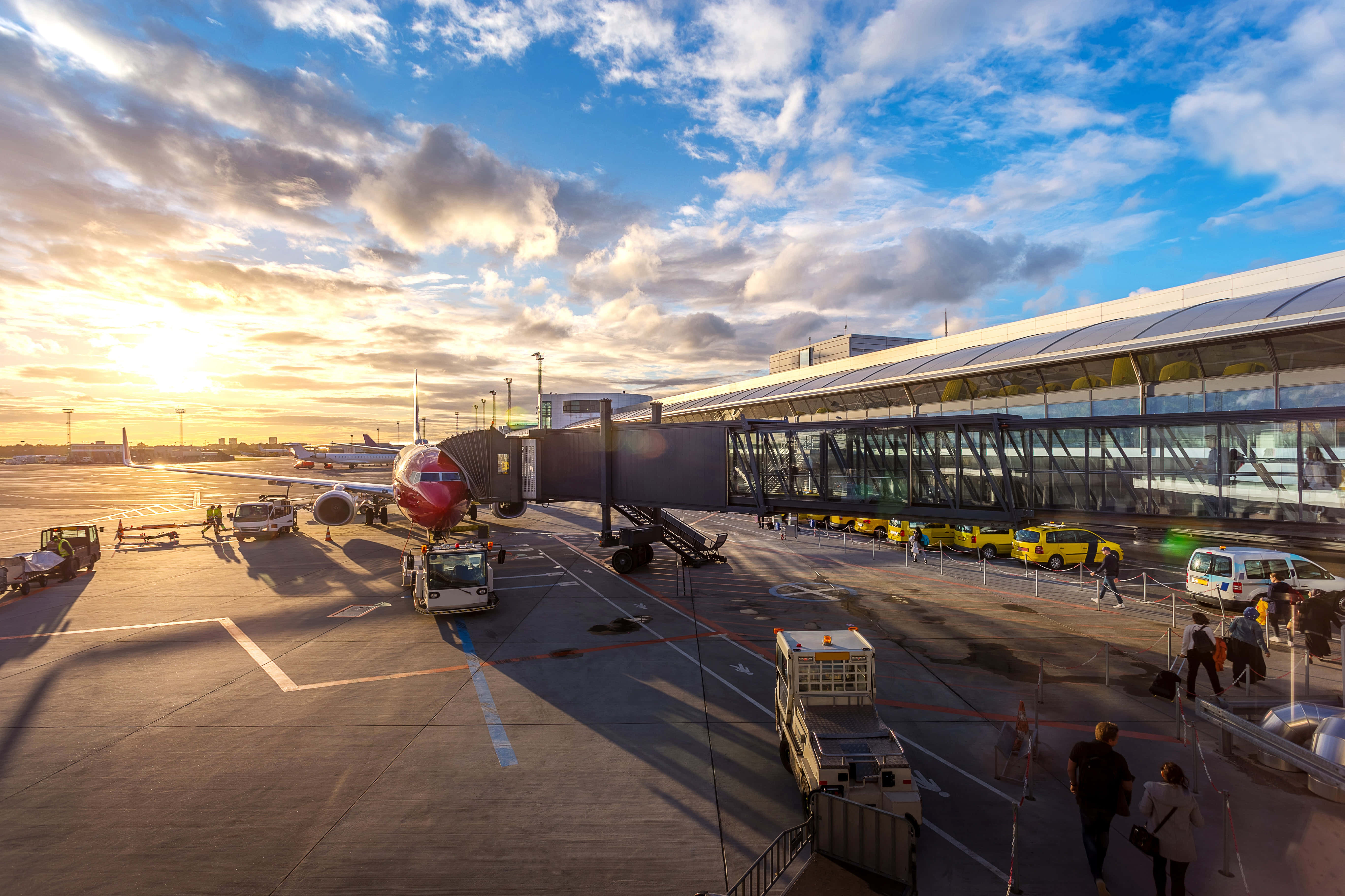 Airport 桌布 壁紙 — 夕陽將機場停機坪沐浴在金色光芒中，乘客們走向一個附近停有紅色飛機的航站樓。