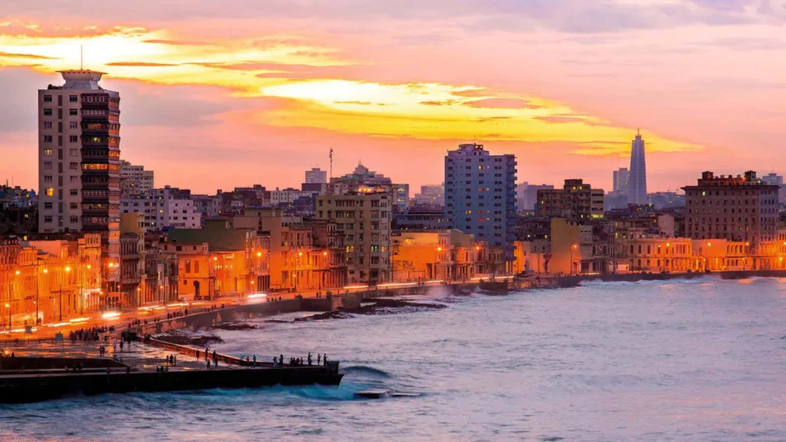Cuba 桌布 壁紙 — 夕陽將海岸城市染上溫暖的橙色和粉紅色，海浪拍打著海岸。