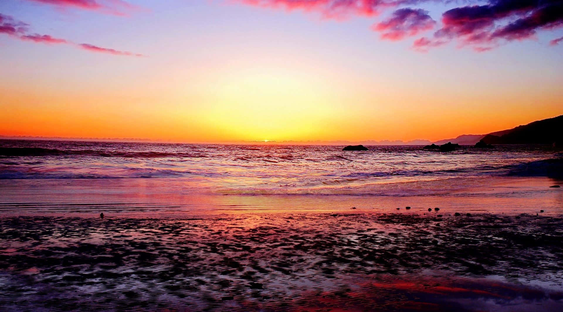 Colorful Sunset 桌布 壁紙 — 夕陽將海洋和天空染成火熱的橙色、粉紅色和紫色，海浪輕輕拍打濕沙灘。