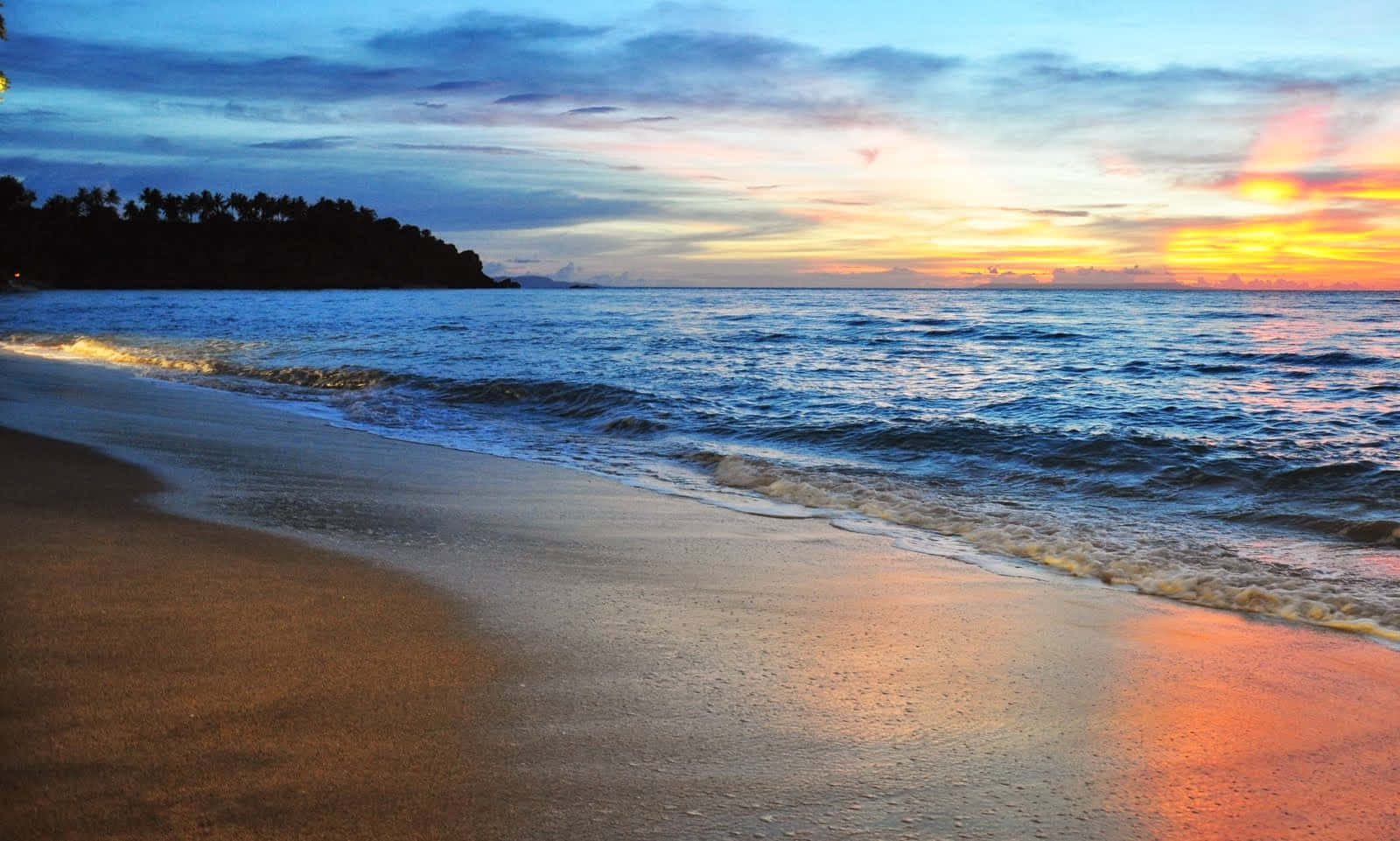 Beautiful Beach 桌布 壁紙 — 夕陽將海洋和沙灘染成溫暖的橙色和清涼的藍色，溫柔的海浪緩緩湧入。