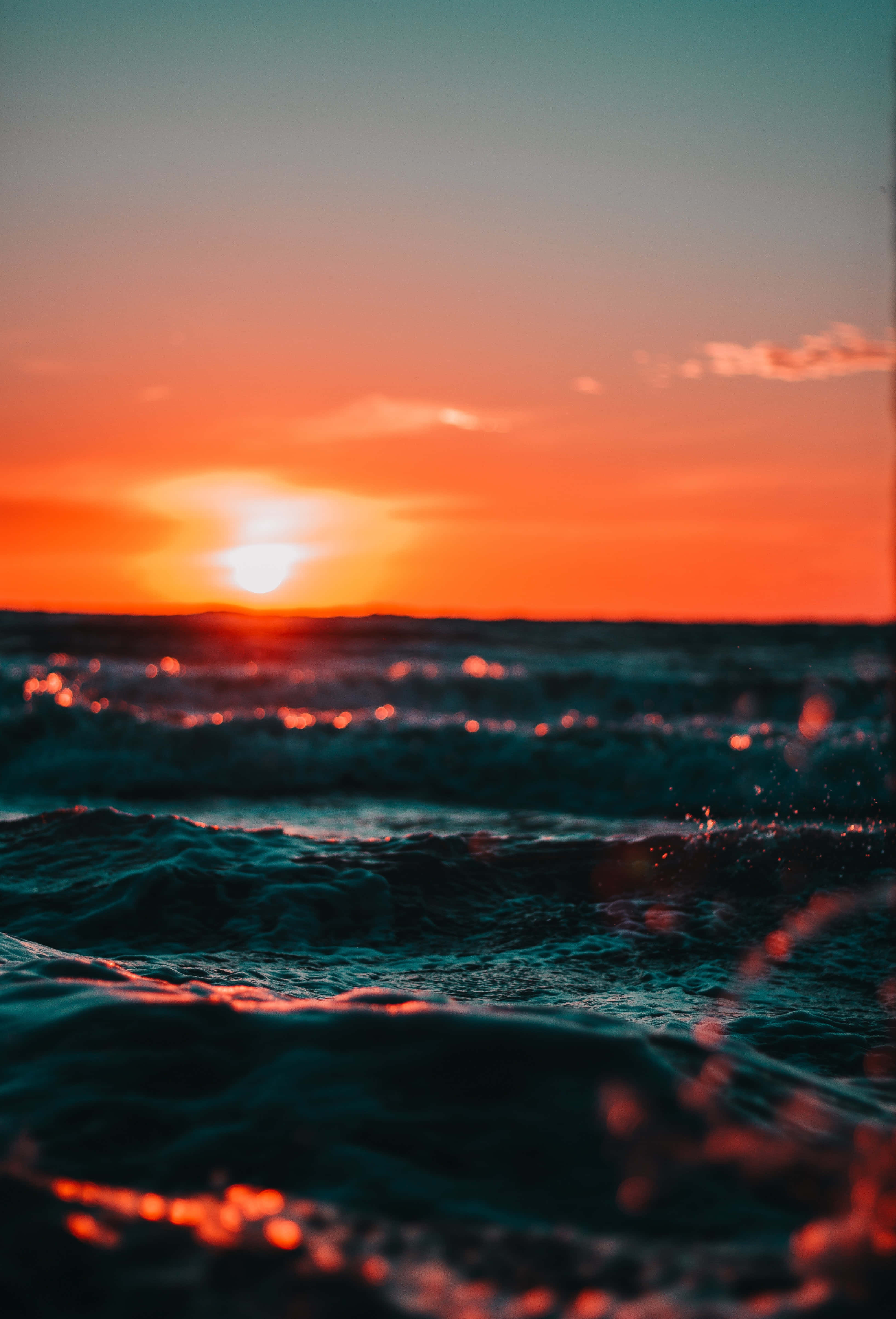 Sunset Wave 桌布 壁紙 — 夕陽將海洋染成火熱的橙色和藍綠色，海浪拍打時閃爍著粼粼波光。