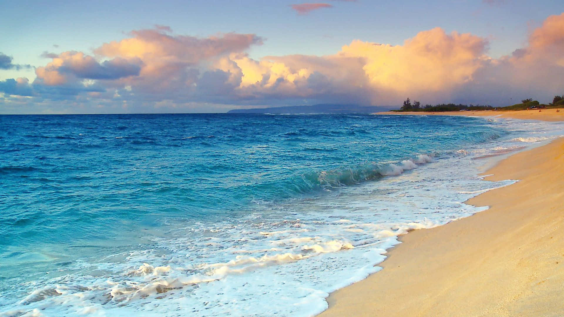 Hawaiian Beach 桌布 壁紙 — 夕陽將蓬鬆的雲朵染成金色，而藍綠色的海浪拍打著金色的沙灘。