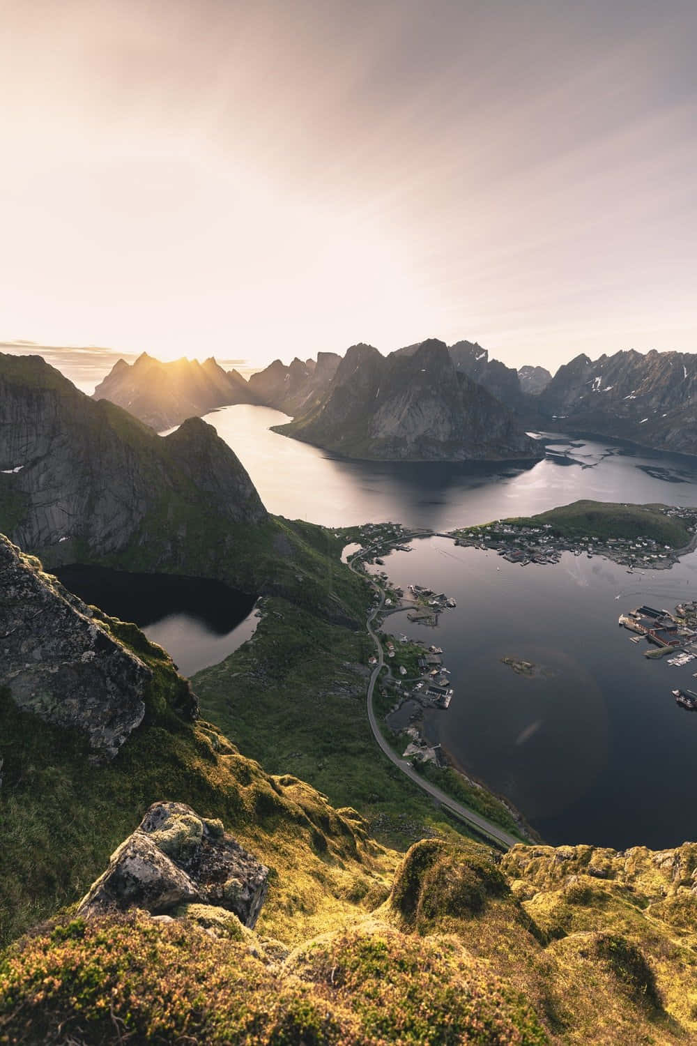 Norway 桌布 壁紙 — 夕陽將鋸齒狀的山脈和蜿蜒的海岸道路沐浴在金色光芒中，照耀著寧靜的峽灣村莊。
