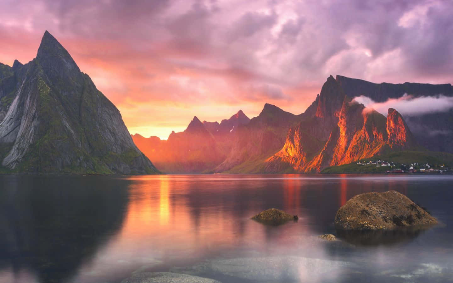Picturesque 桌布 壁紙 — 夕陽將鋸齒狀的山脈染成火熱的橙色和紫色，它們的倒影在平靜的水面上閃耀，水中有漂浮的岩石。
