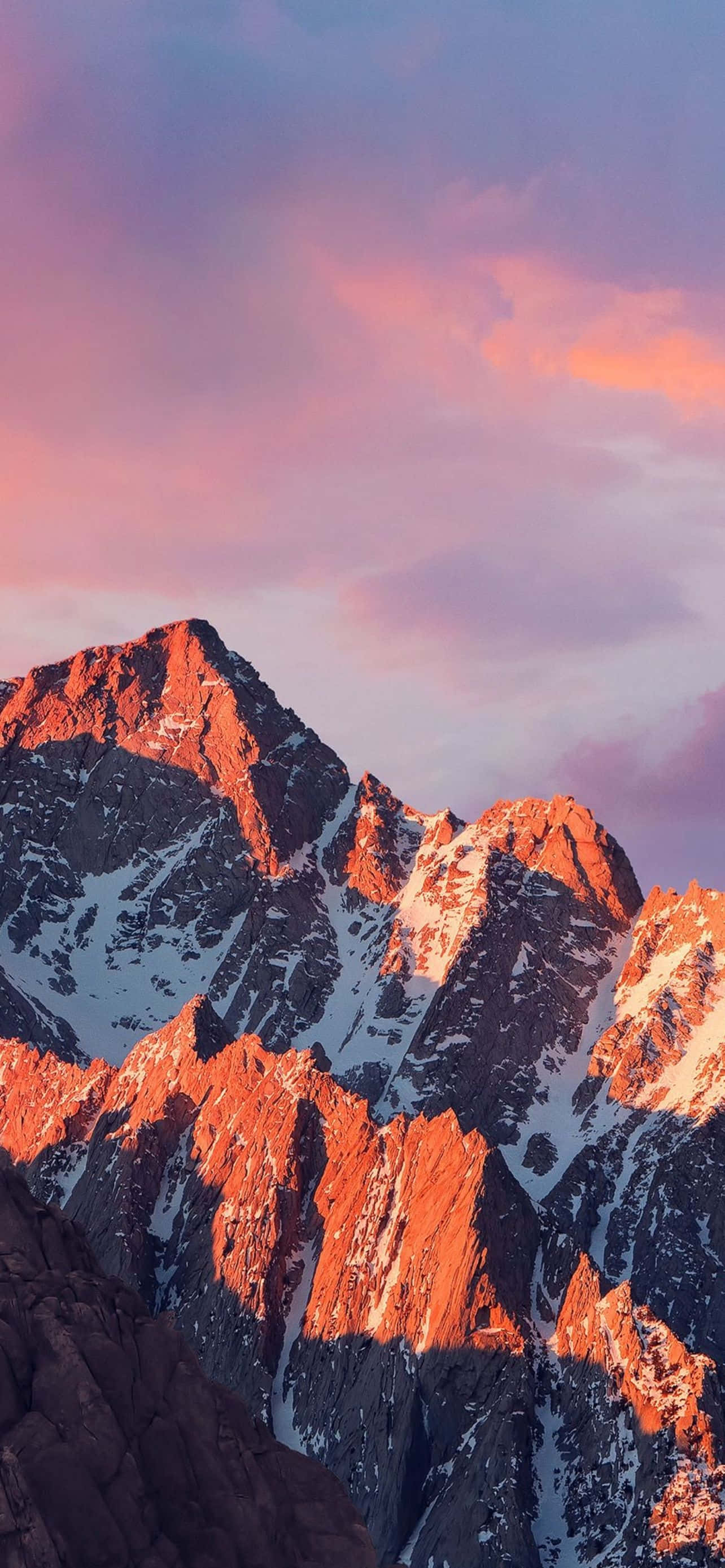 Mountain iPhone 桌布 壁紙 — 夕陽將鋸齒狀的雪山山頂染成火橙色，映襯著柔和的粉紫色天空。