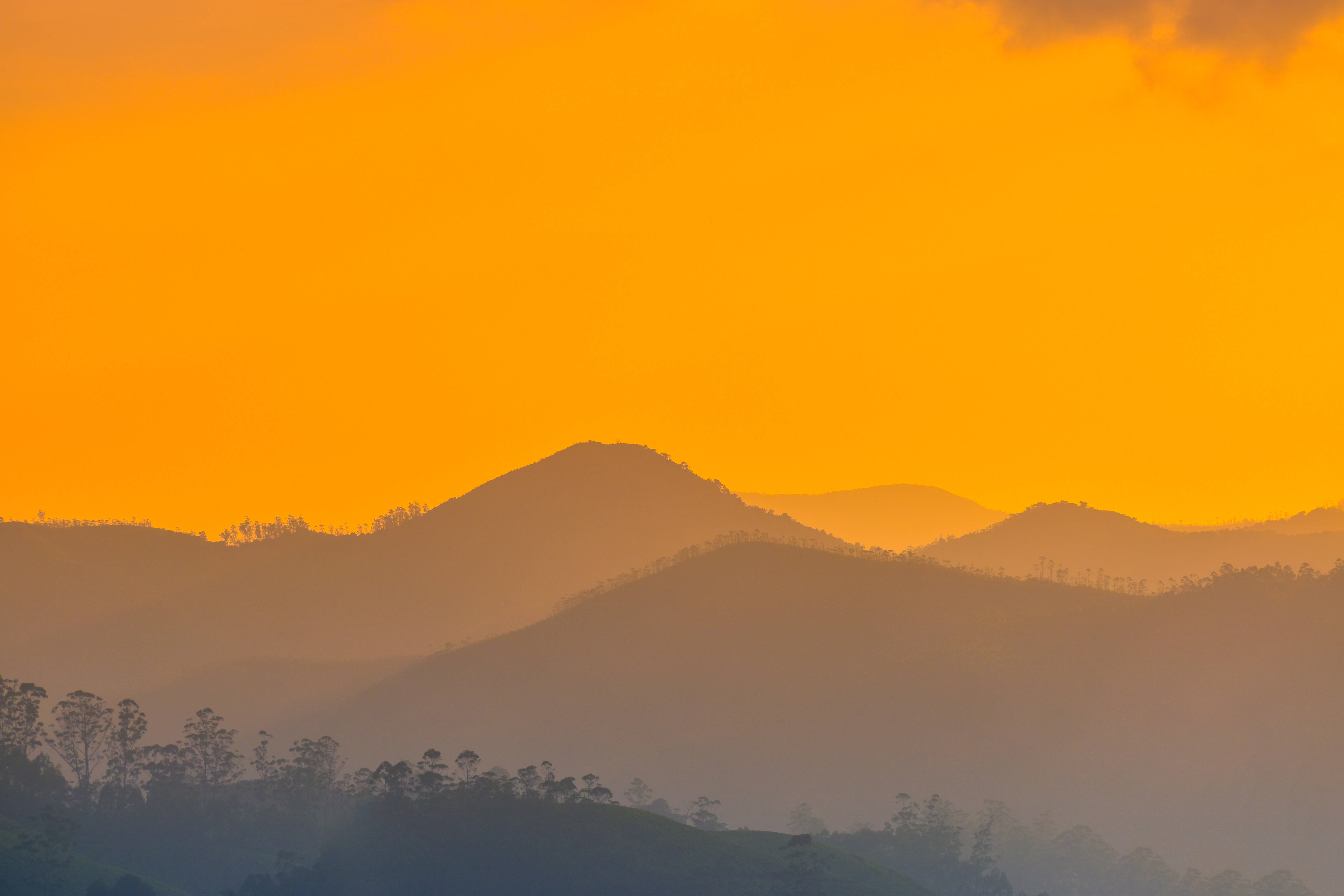 夕陽山景筆電壁紙 壁紙 — 剪影般的山脊在日出天空朦朧的橙色光芒中逐漸消失。