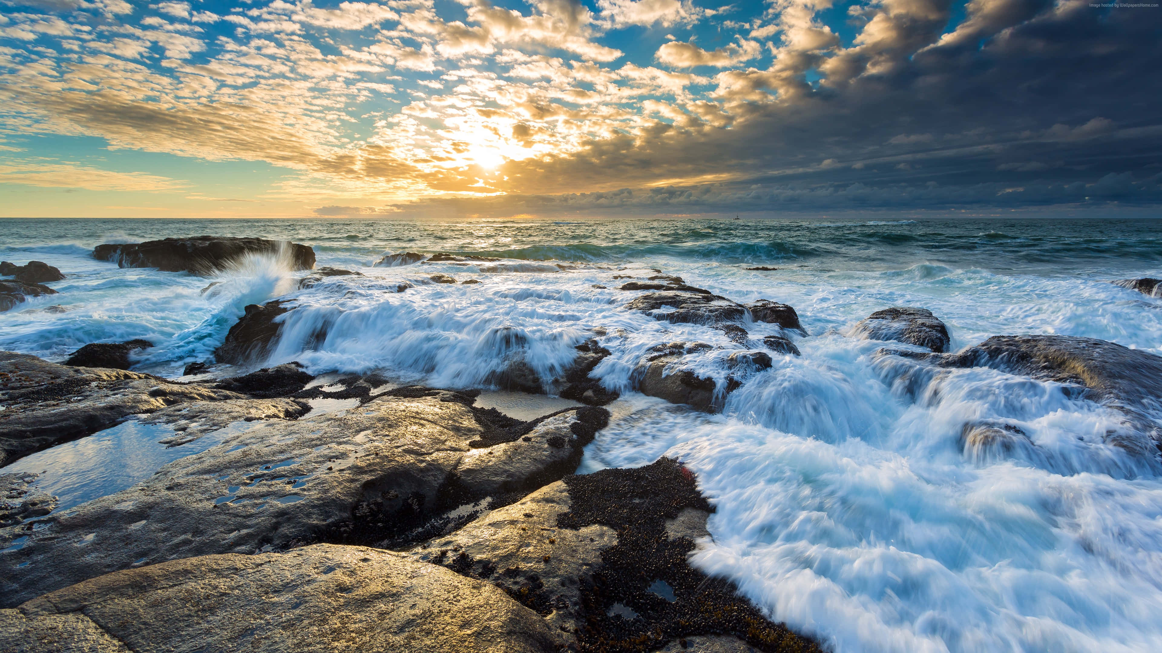 Beach Photography 桌布 壁紙 — 夕陽描繪出戲劇性的雲彩，海浪拍打著崎嶇的海岸岩石，激起水花。