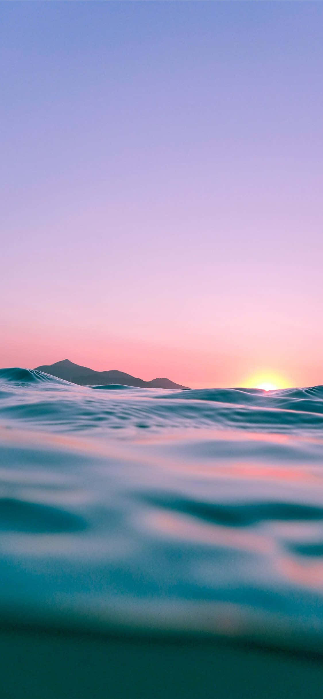 夕陽映照海浪與山巒的海洋 壁紙
