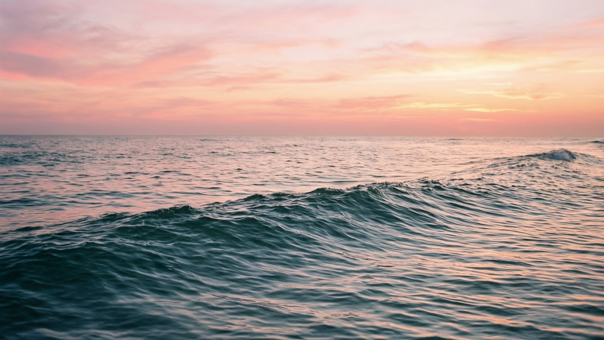 夕陽海景寧靜 壁紙 — 在柔和粉紅與橙色的日落天空下，平靜的海浪翻滾。